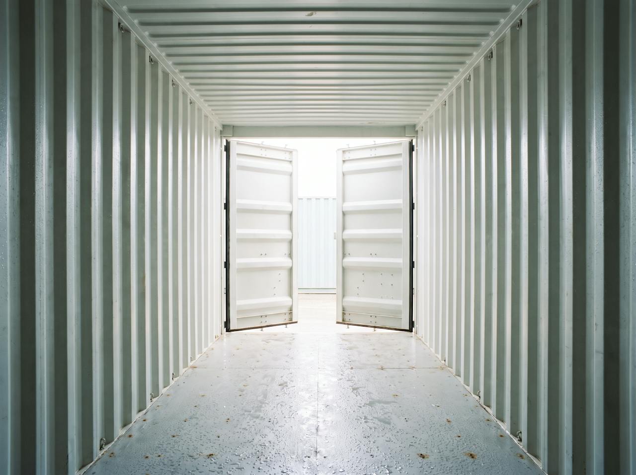 Inside a bare shipping container on a cold morning: the corrugated steel walls and roof beaded with condensation, a run of drips on the floor and rust starting along a lower seam.