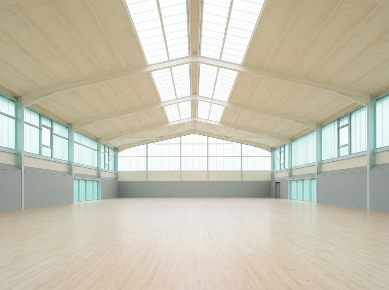 The same roof after treatment: a continuous cream closed-cell layer with a pale coating on its face, following the sheet between the beams above the pool.
