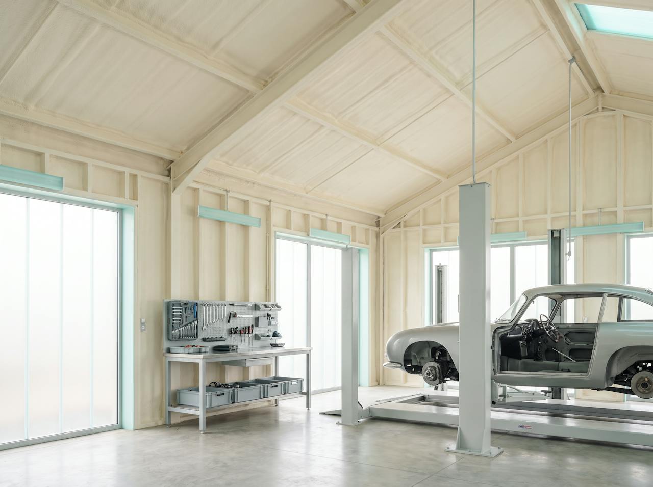 The same workshop after treatment: a continuous cream closed-cell layer on the roof underside running down the inside of the steel-clad wall to the bench height.