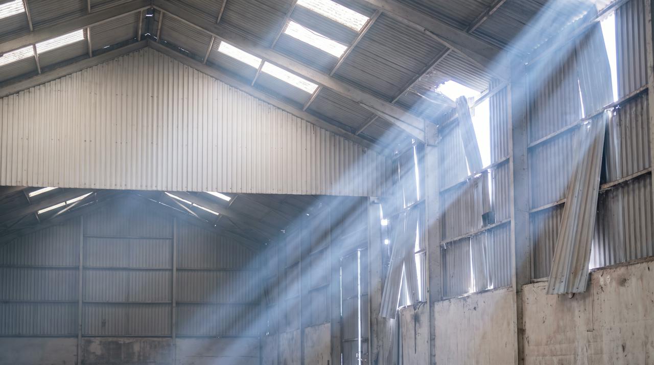 Daylight showing through the open laps and eaves of a bare profiled metal roof, seen from inside a cold building.