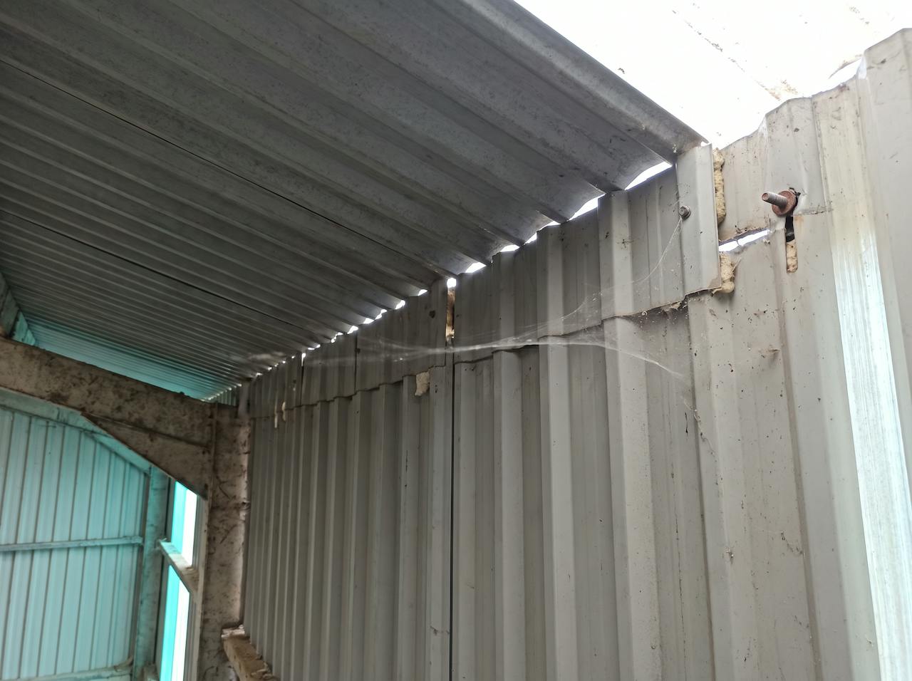 Close view of a profiled steel roof underside near the eaves: an open side lap with daylight showing through, a rusted fixing and a crumbled foam filler.
