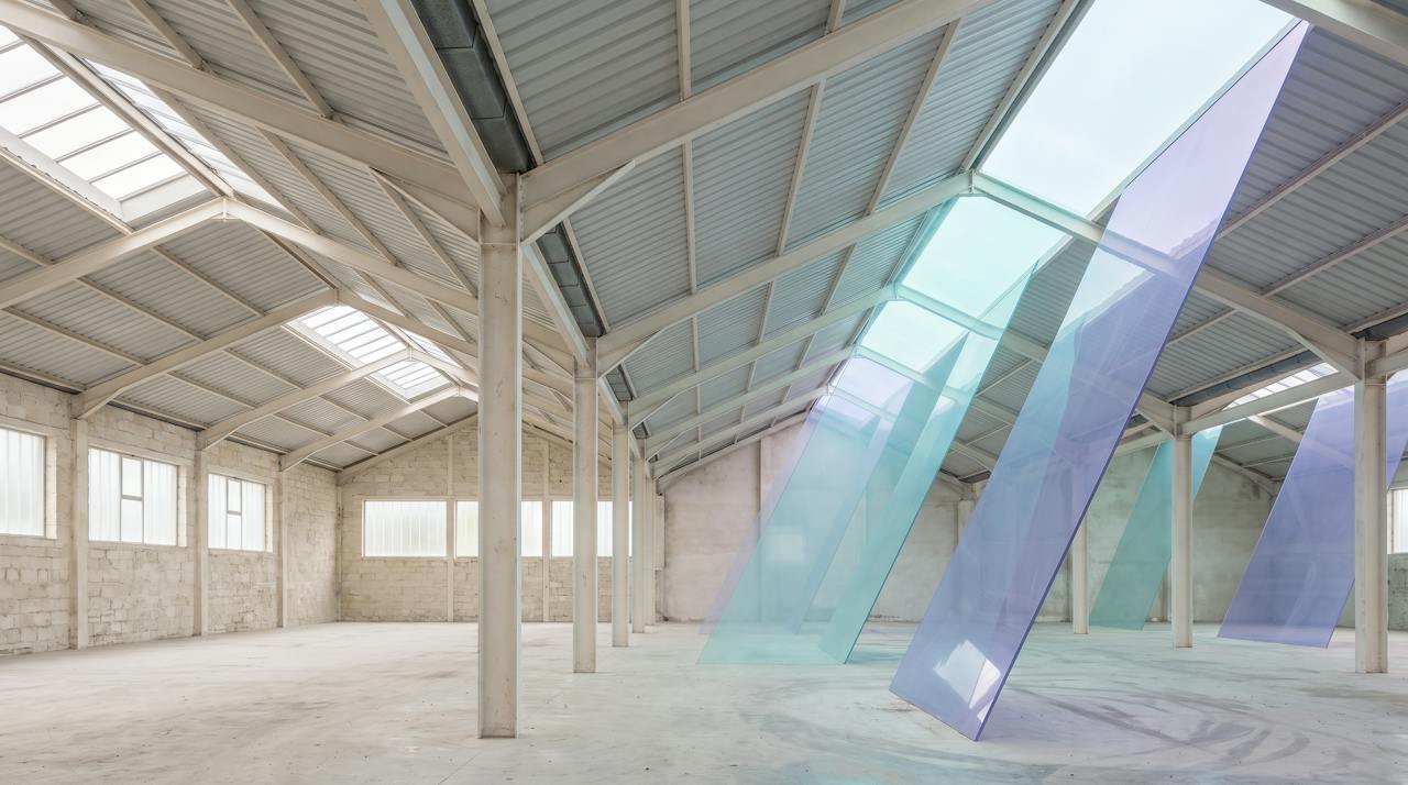 A pale industrial roof interior in which planes of warm violet and aqua light rise through the roof, the heat leaving upward through a bare sheet.