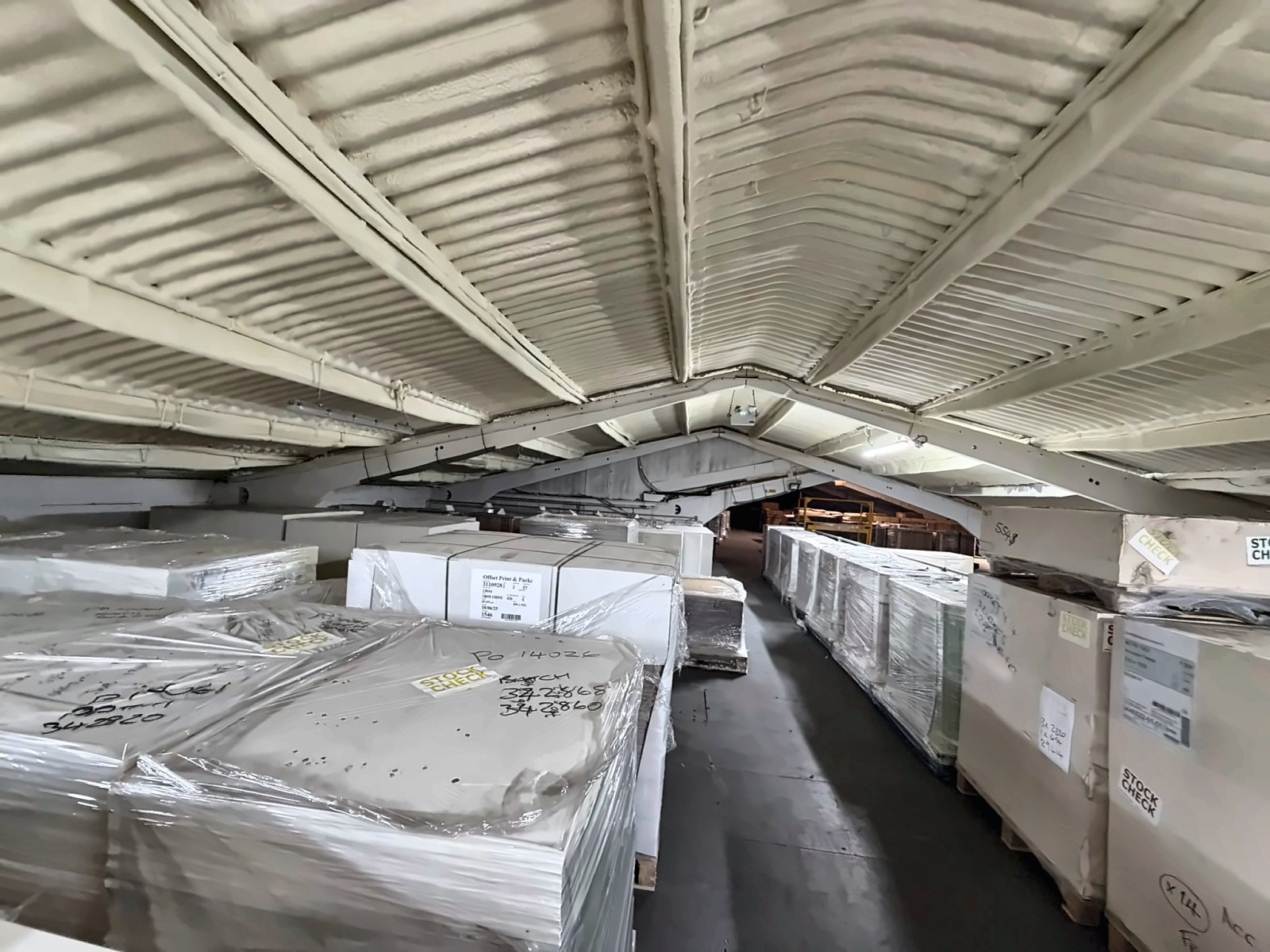 A storage building roof sprayed from beneath above palletised, wrapped stock.