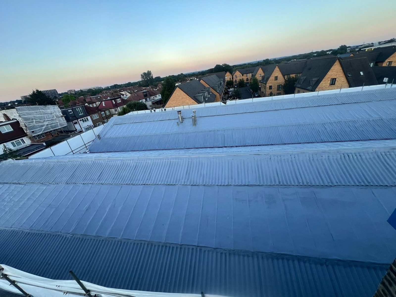 The four pitched roofs of Global House after the work, at dusk, under one continuous coated surface.