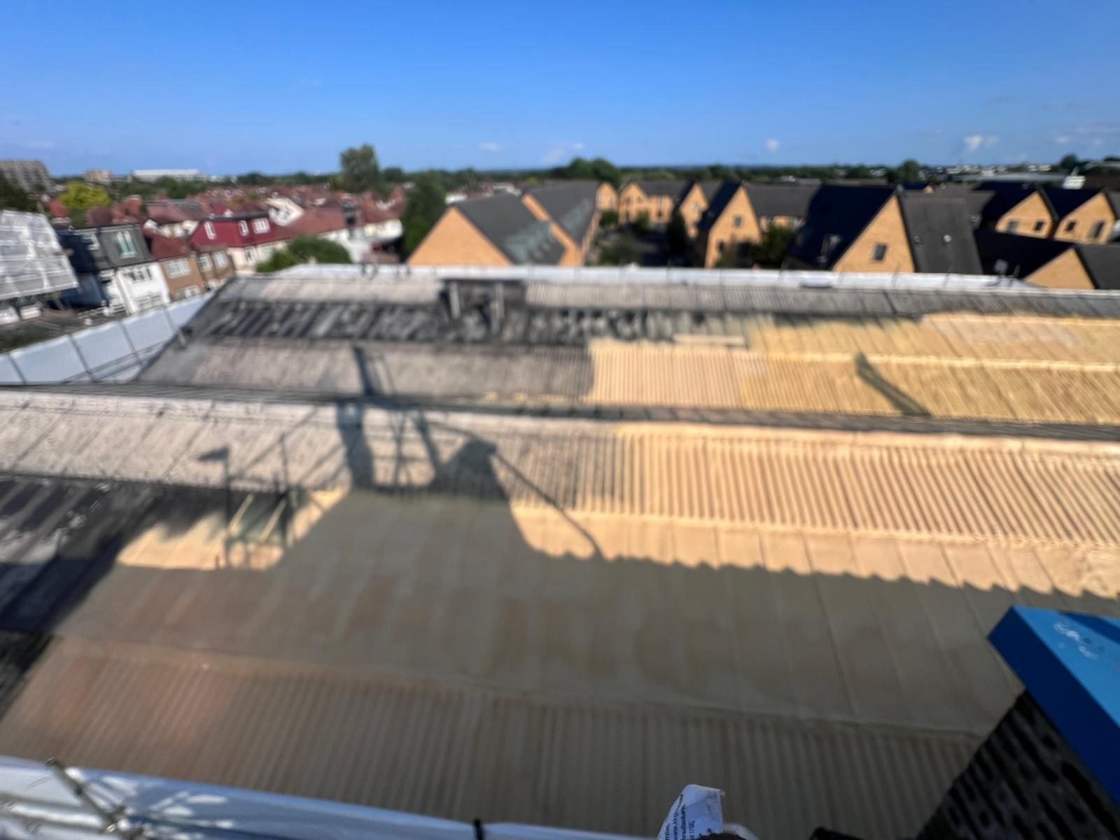 During the work at Global House: closed-cell roofing foam being sprayed over the washed asbestos-cement sheets, the corrugations filling under a continuous layer.