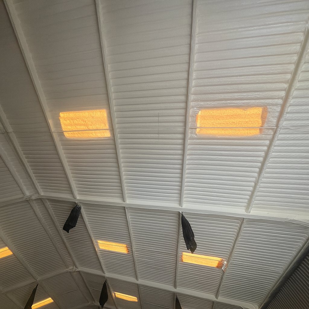 Inside the TJW Grab Hire warehouse after the work: the box-profile roof under a continuous closed-cell layer, rooflights left clear.