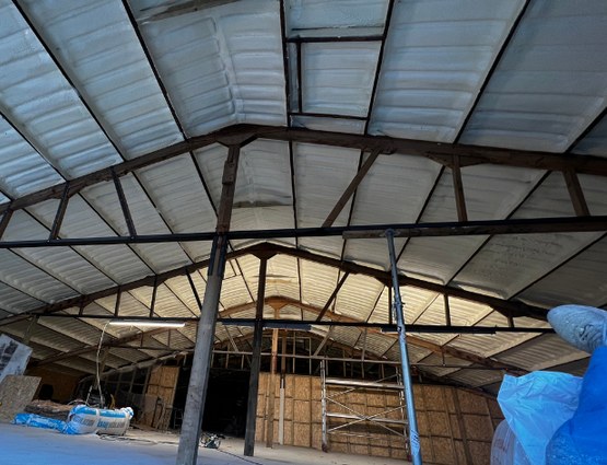 Inside the Midlands warehouse after the work: the corrugated metal roof and its trusses under a continuous cream closed-cell layer.