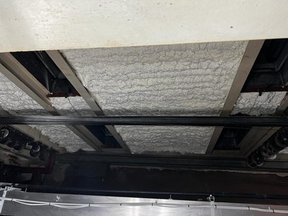 The sprayed roof deck above the fly tower: white open-cell foam filling the bays between steel beams and the steelwork left exposed beneath it.