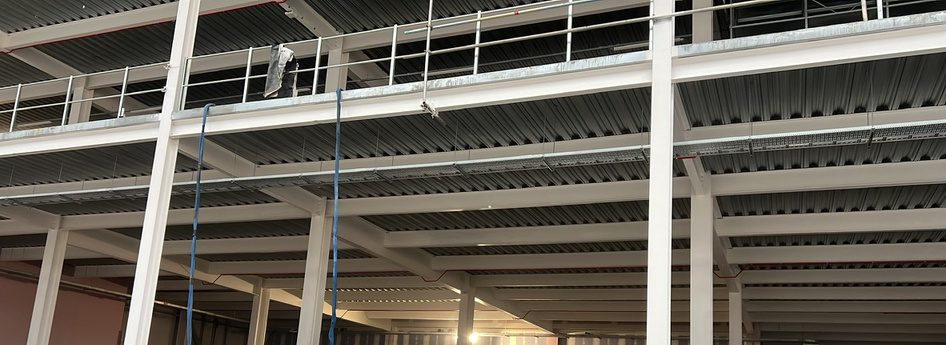 Before: the new warehouse frame with the bare profiled steel decking exposed on the underside of the mezzanine deck, pale painted beams and columns below it.