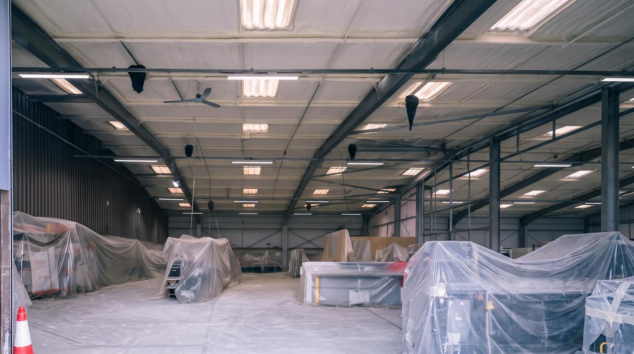A factory roof under a continuous closed-cell layer, the machinery below wrapped in protective polythene sheeting.