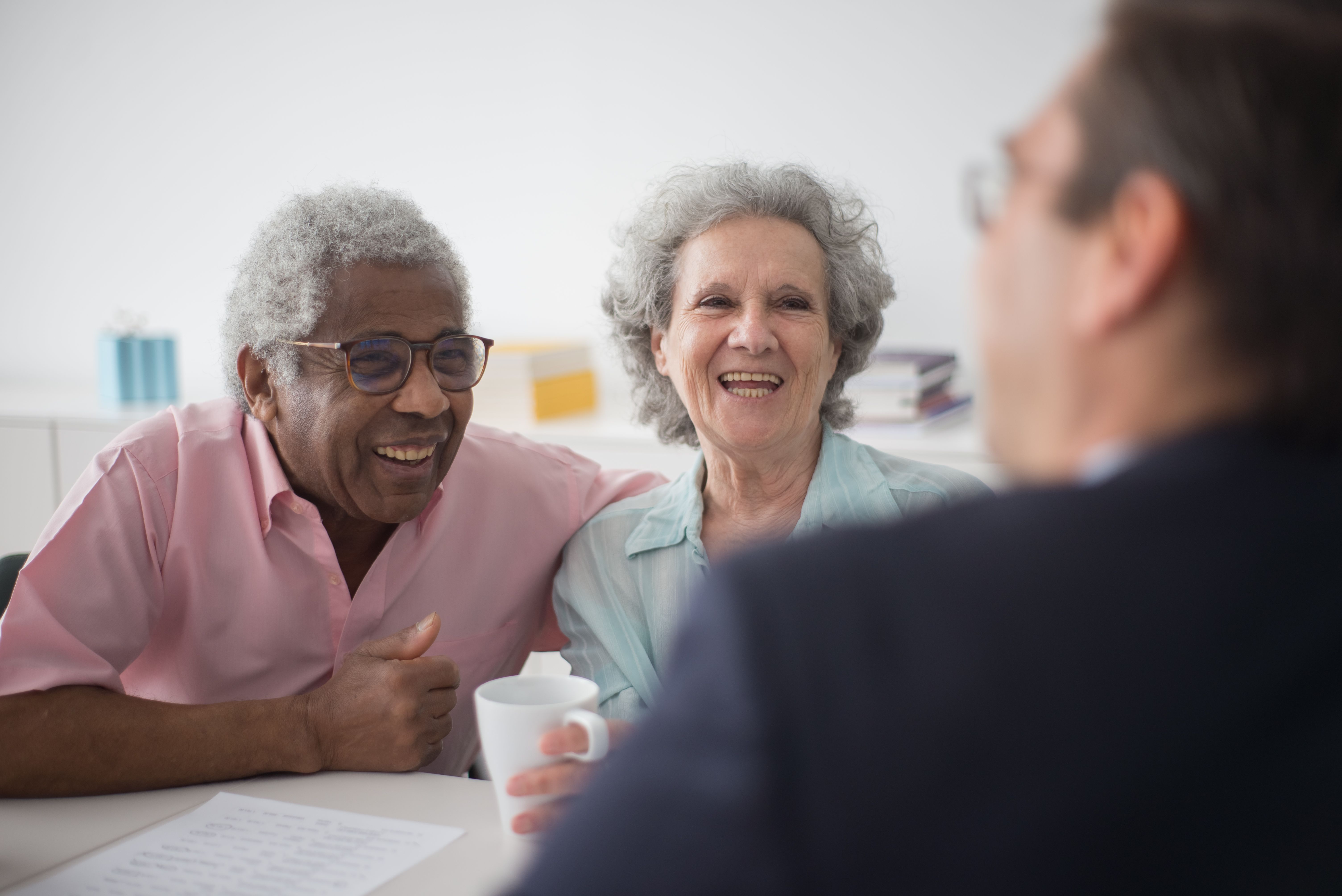 Smiling older couple talking with a man, seated at a table with a document and coffee cup.
