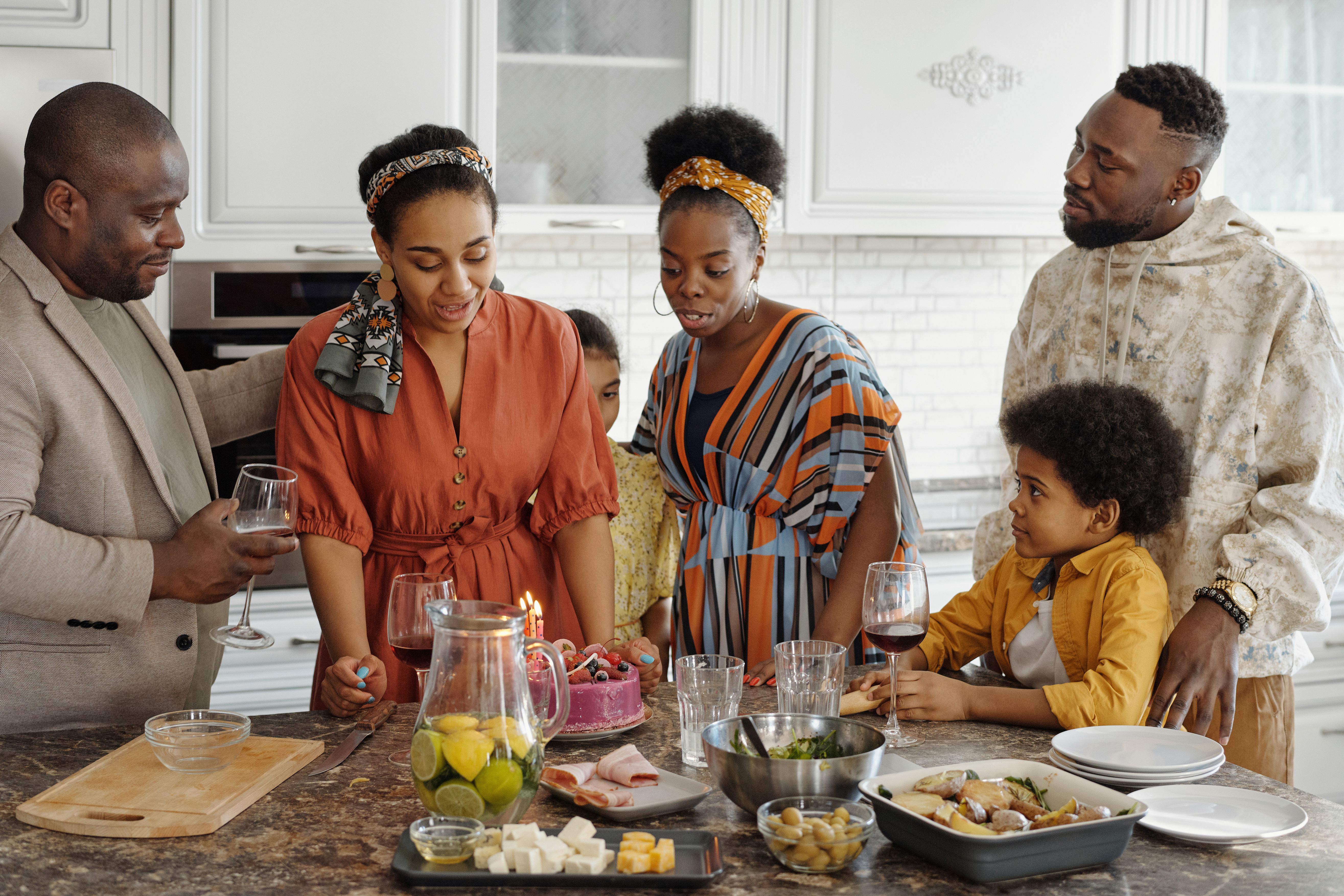 Family gathered around a kitchen island celebrating a birthday with cake candles lit and food on the counter.