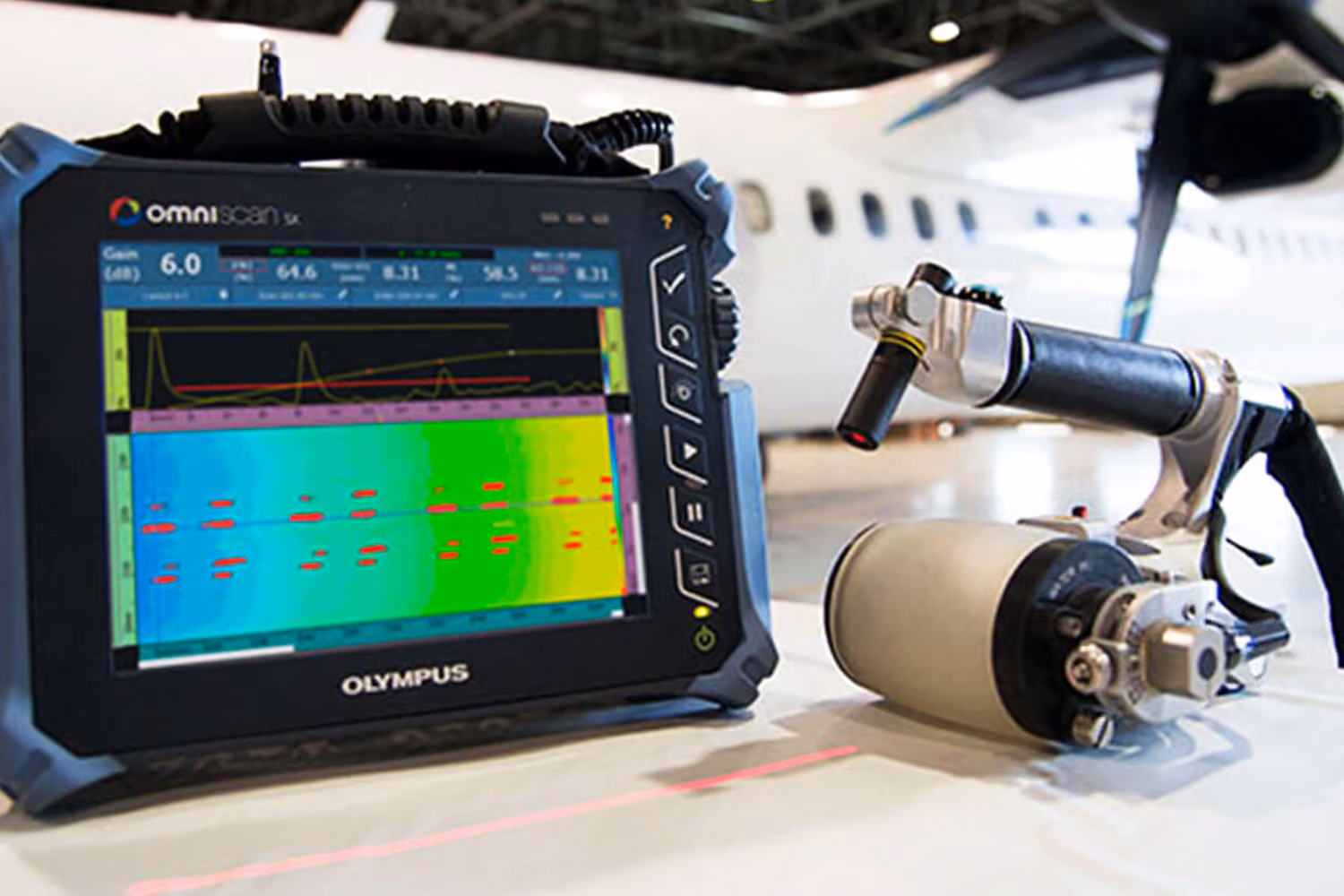 OmniScan SX device with graph display and sensor next to an airplane in a hangar.