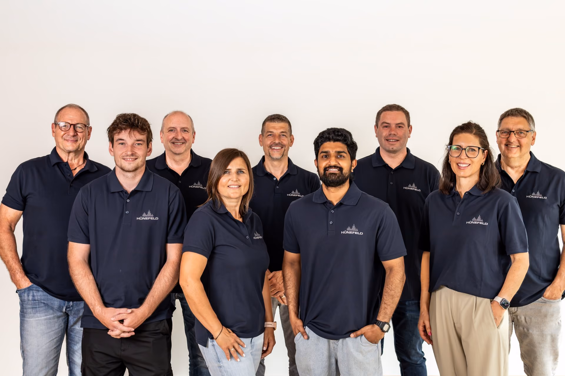 Gruppenfoto von neun Personen in blauen Hünefeld-Poloshirts vor weißem Hintergrund.