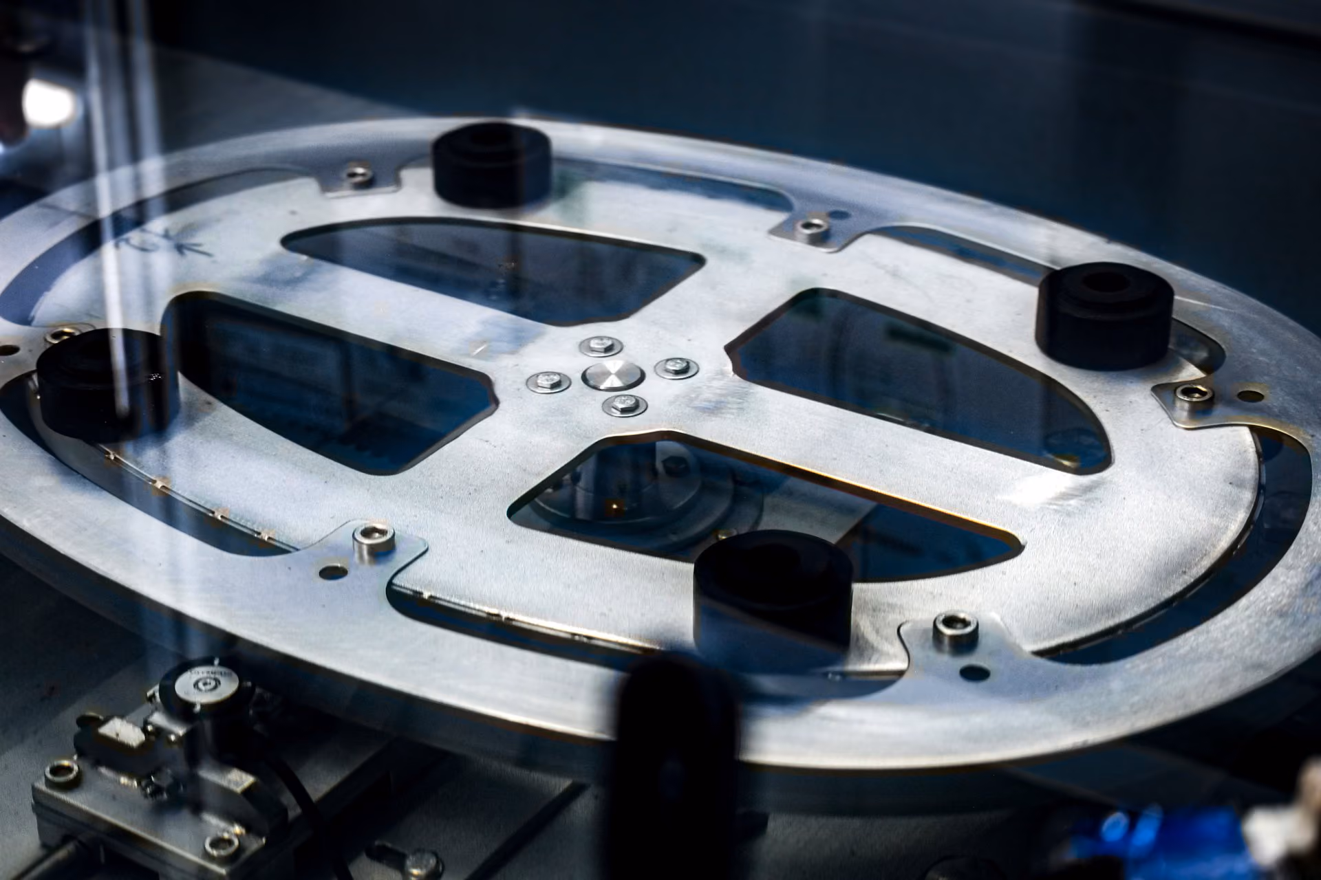 Metallplatte mit ovalen Ausschnitten auf technischer Prüfmaschine mit schwarzen Dämpfern.