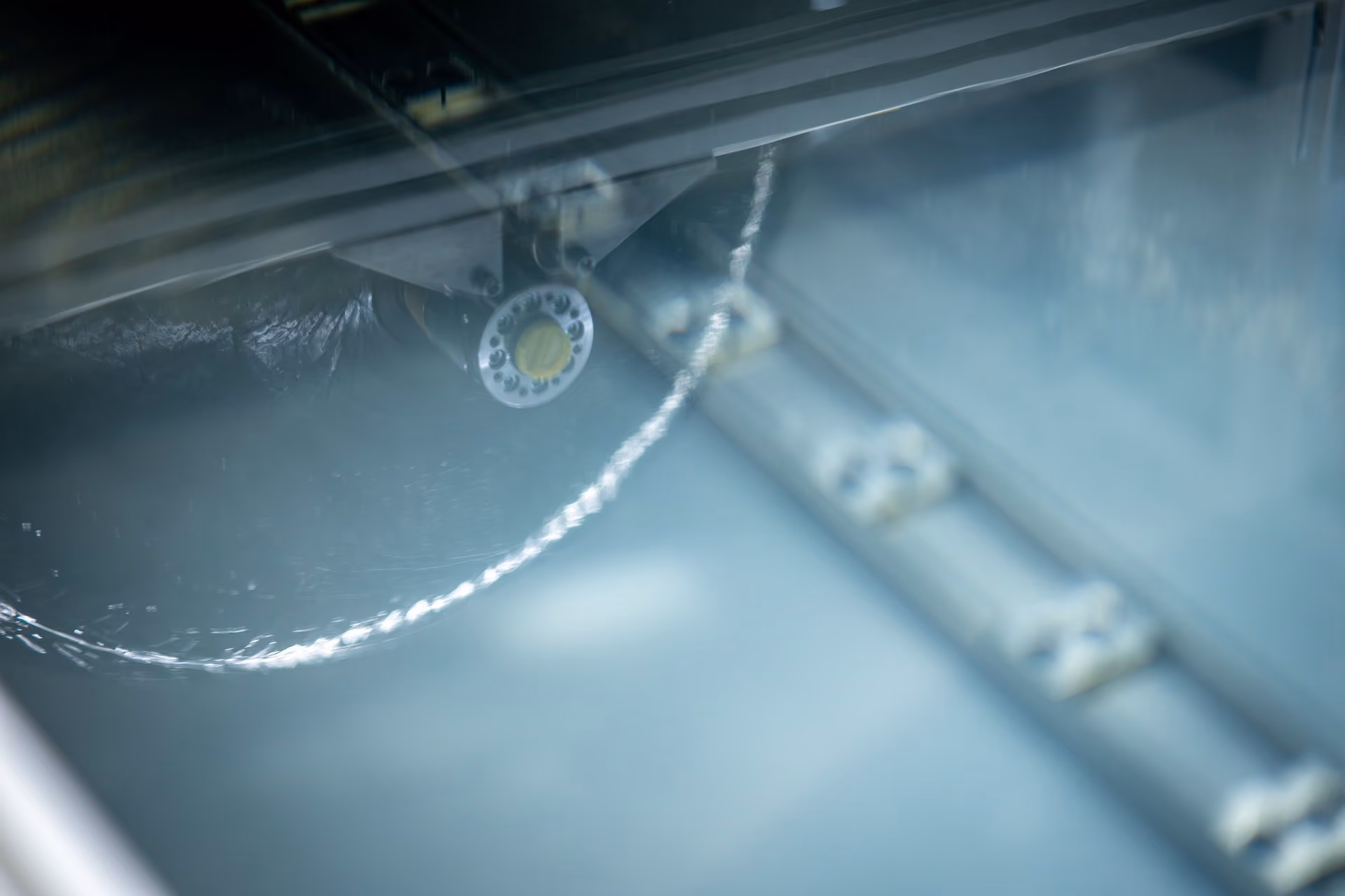 Nahaufnahme eines Wasserstrahls aus einer Metallanlage, der in einem Wasserbad fließt.