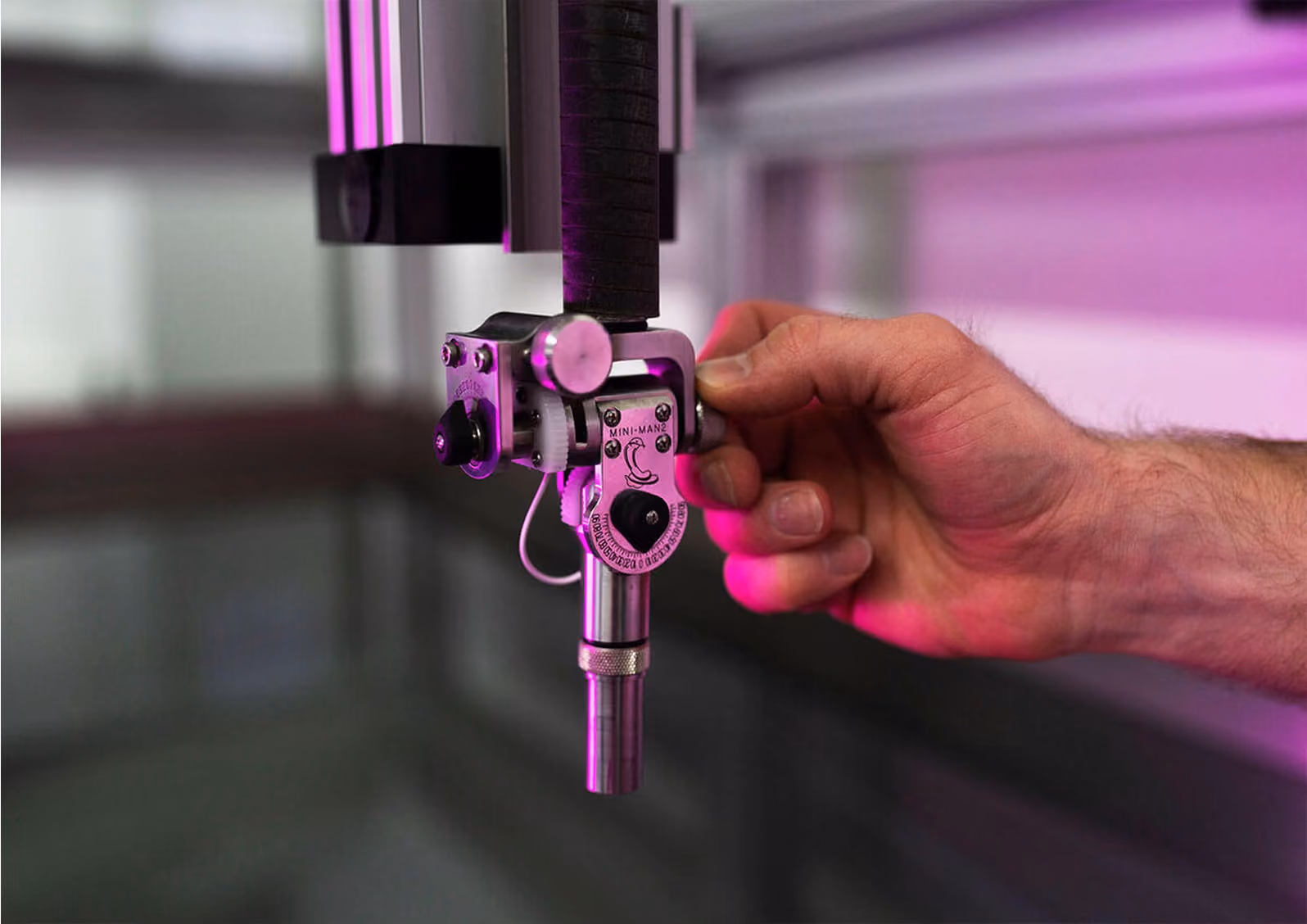 Hand adjusting a small mechanical device with MINI-MAN2 label under purple lighting.
