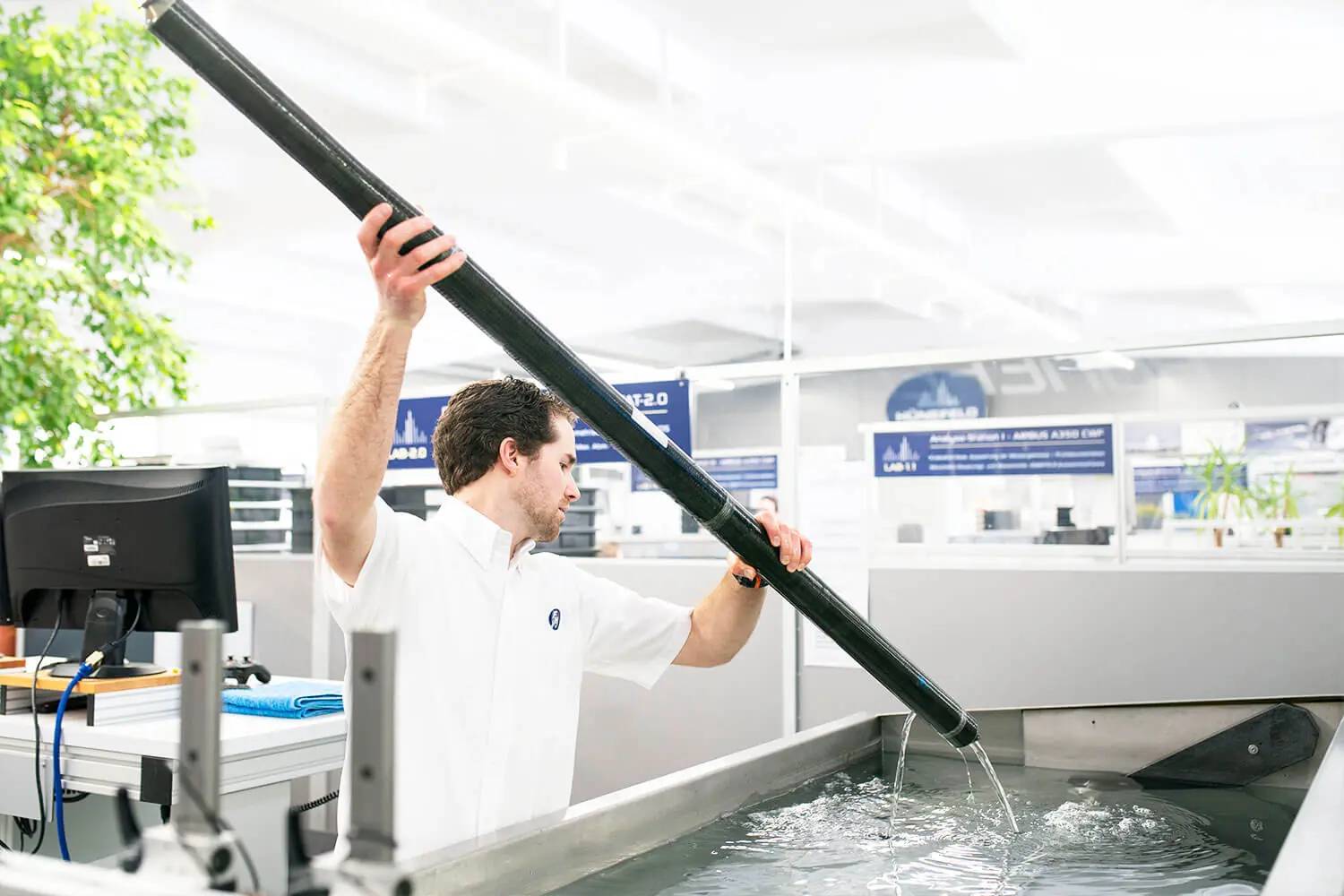 Mann hält großen schwarzen Schlauch und lässt Wasser in ein Wasserbecken fließen in moderner Büroumgebung.