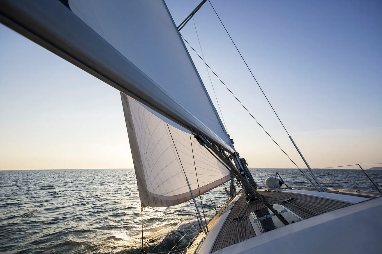 Segelboot segelt bei klarem Himmel und ruhiger See mit Sonnenschein auf dem Wasser.