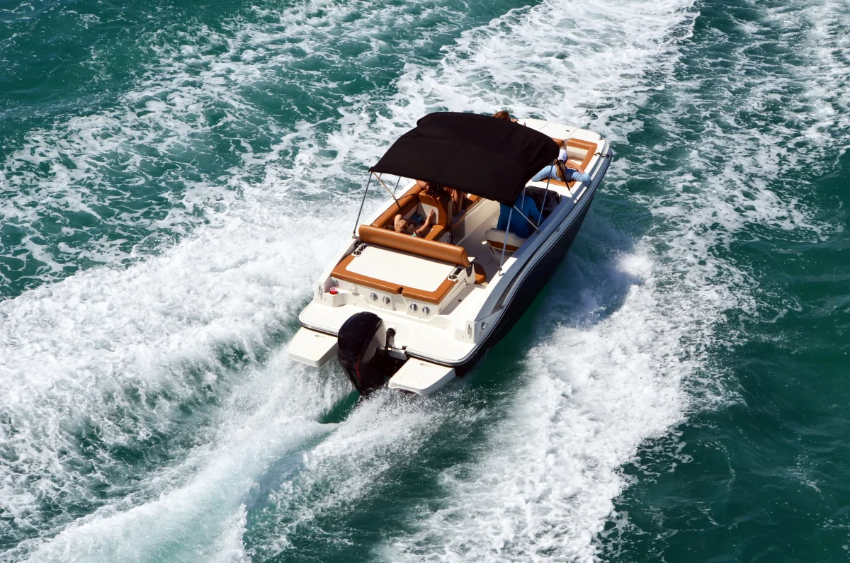 Motorboot mit schwarzem Verdeck fährt auf blauem Wasser und erzeugt weiße Gischt.
