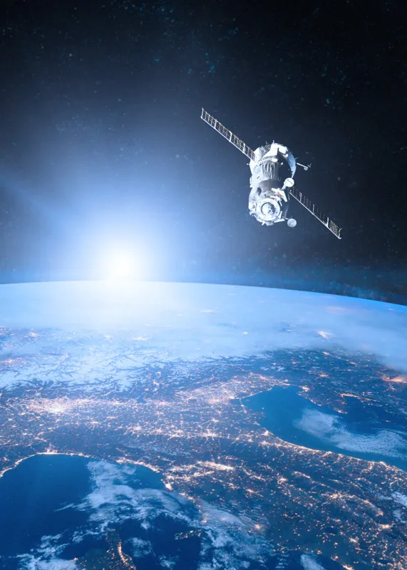 Satellit im Orbit über der Erdoberfläche mit vielen Stadtlichtern und Sonnenaufgang am Horizont.