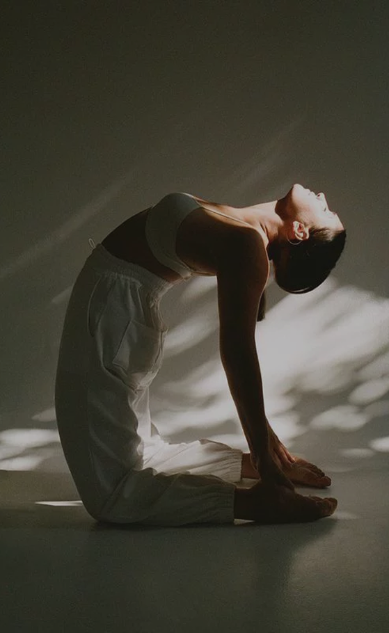 Mujer en postura de camello de yoga bajo luz natural