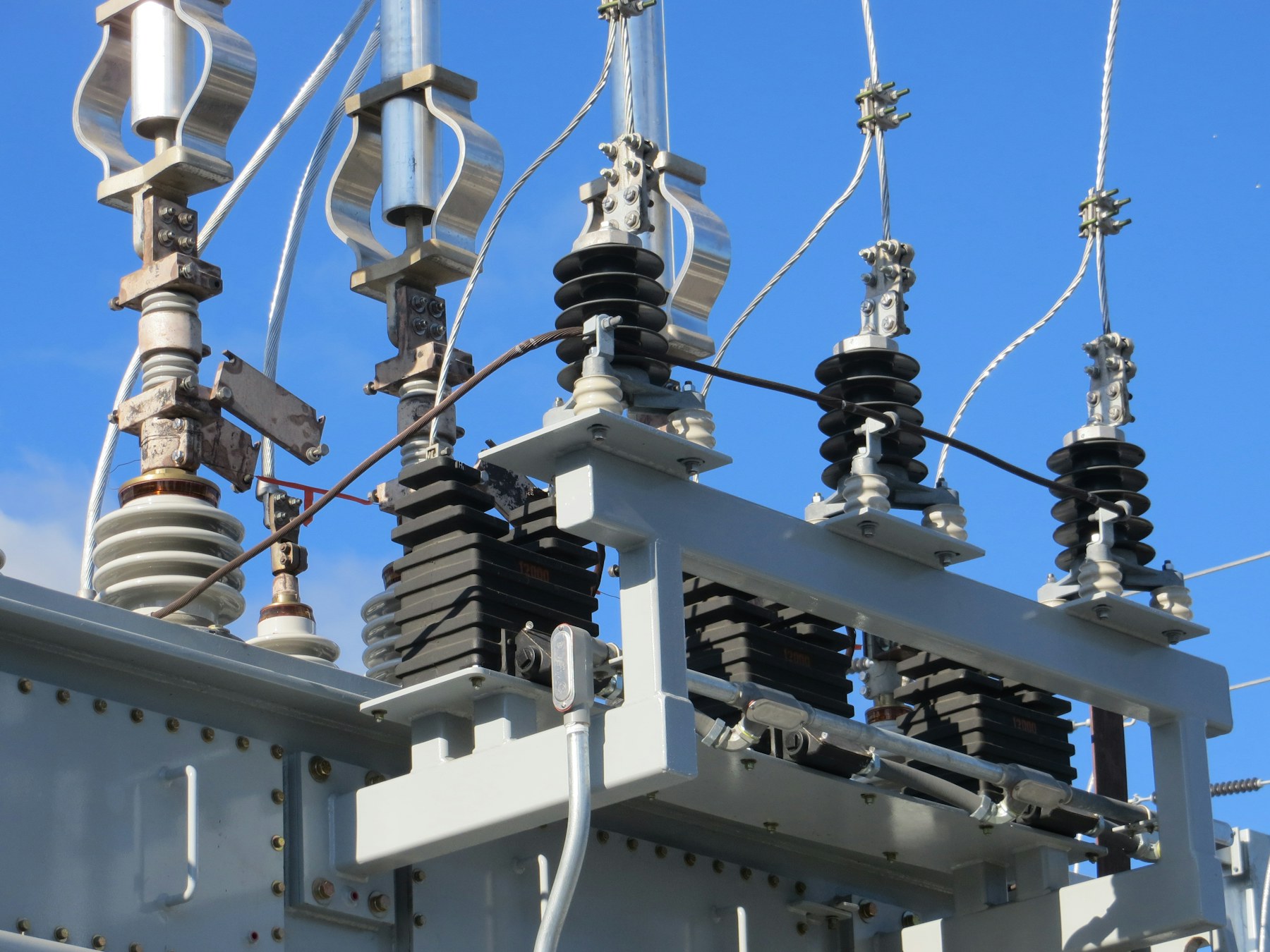 Cyber-Blackout-Übung bei einem Stadtwerk – Elektrische Isolatoren und Metallkomponenten an einem Transformator vor klarem blauen Himmel