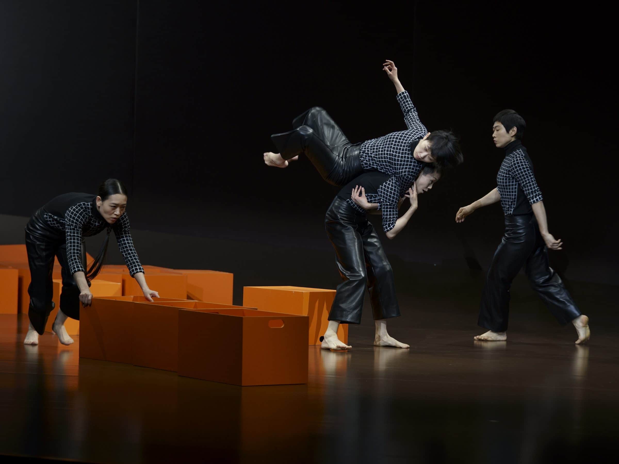 Four dancers in checked shirts move orange boxes across the stage, Hermès show in Shanghai
