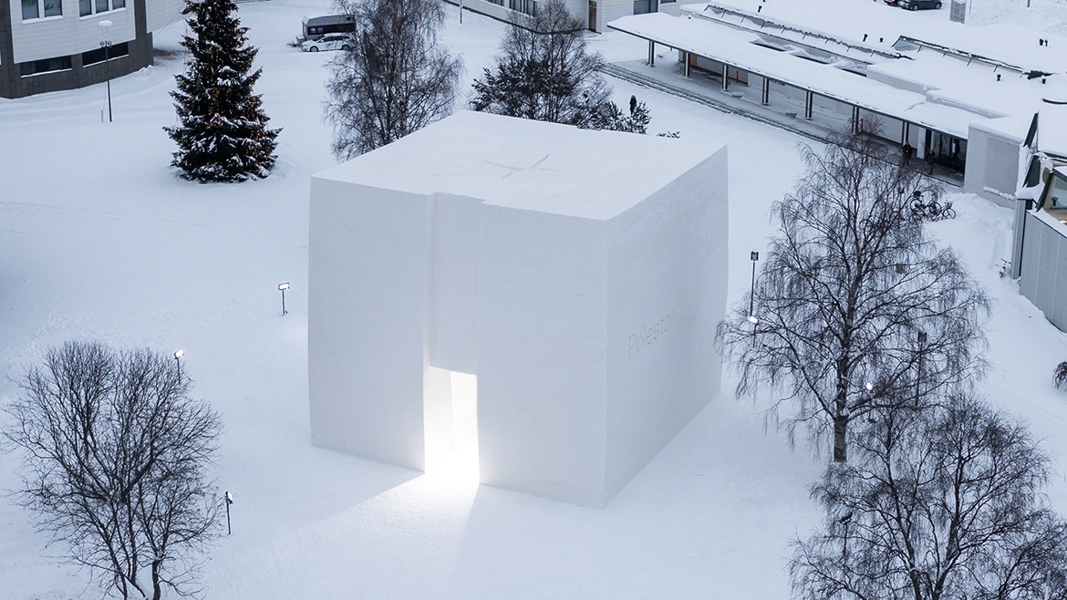 Würfelförmiger Pavillon komplett aus Schnee, umgeben von winterlicher Parklandschaft