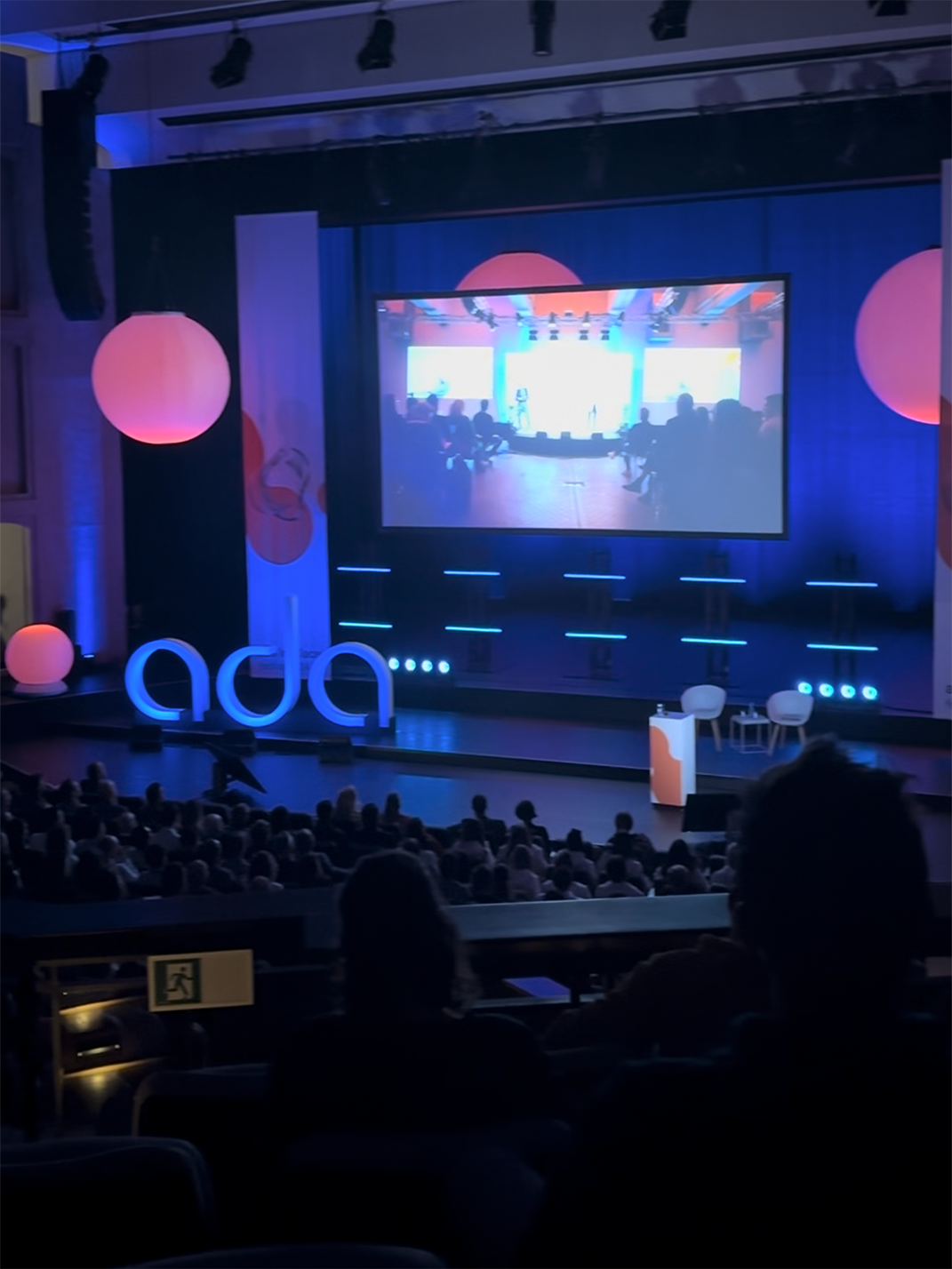 Bühne mit „ada“-Schriftzug und Leuchtkugeln beim Ada Lovelace Festival 2024, im Hintergrund die Leinwand.