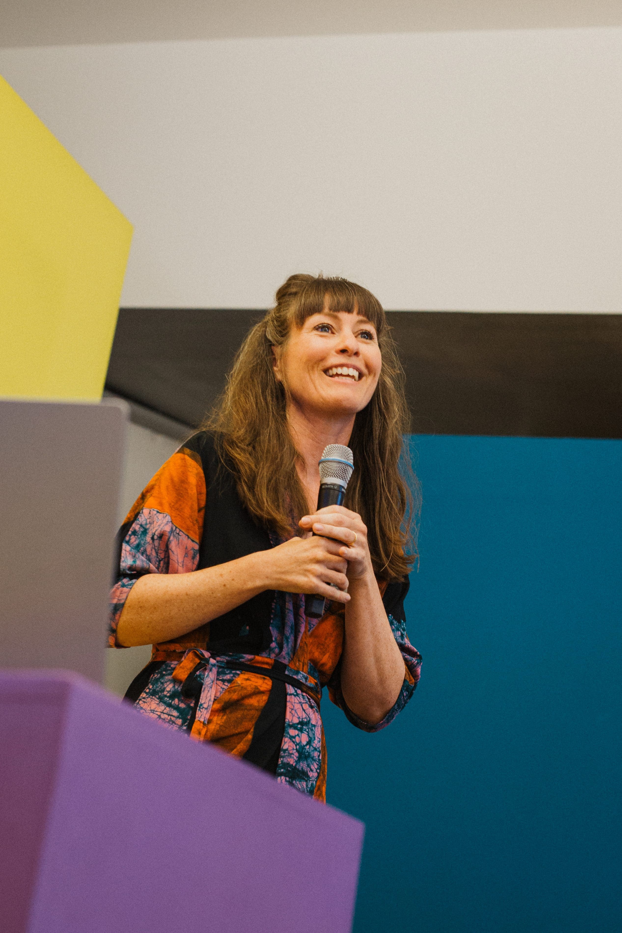 Speakerin mit Mikrofon vor gelber und blauer Wand auf der Bühne beim Salon39