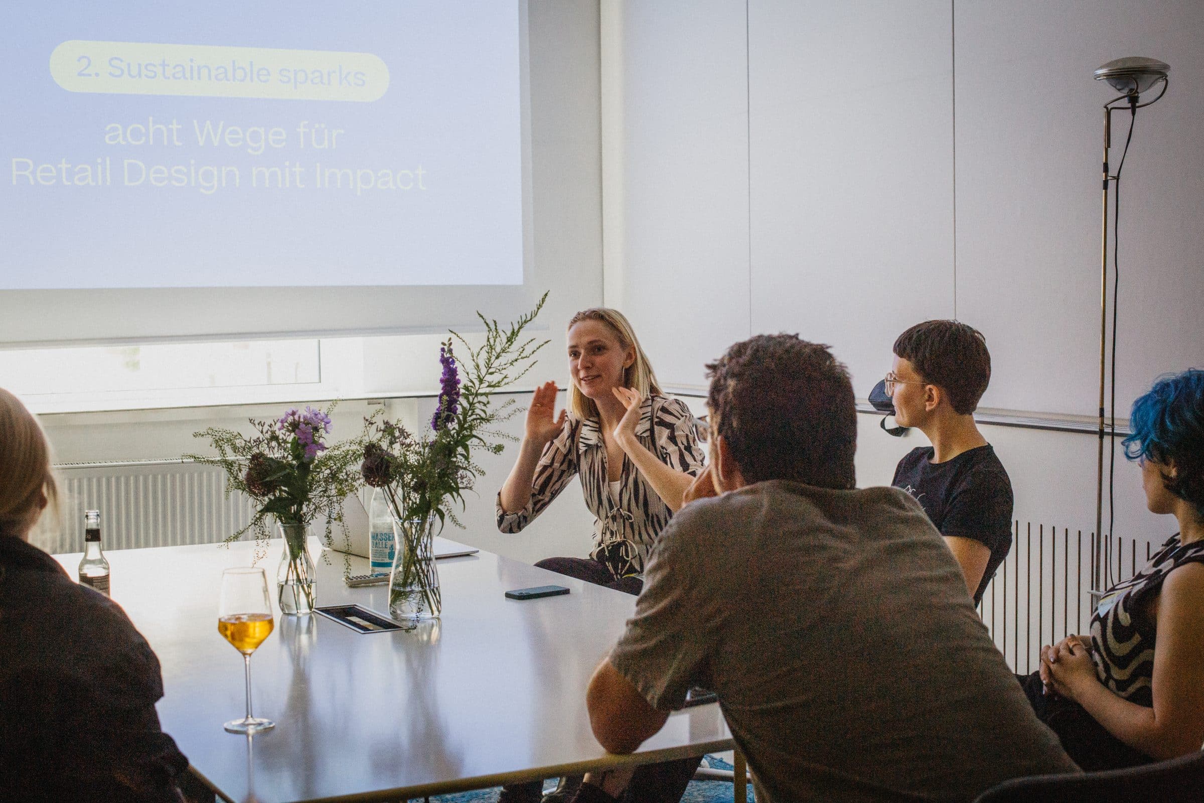 Workshop-Runde am Tisch, im Hintergrund die Folie „Sustainable Sparks – acht Wege für Retail Design mit Impact“