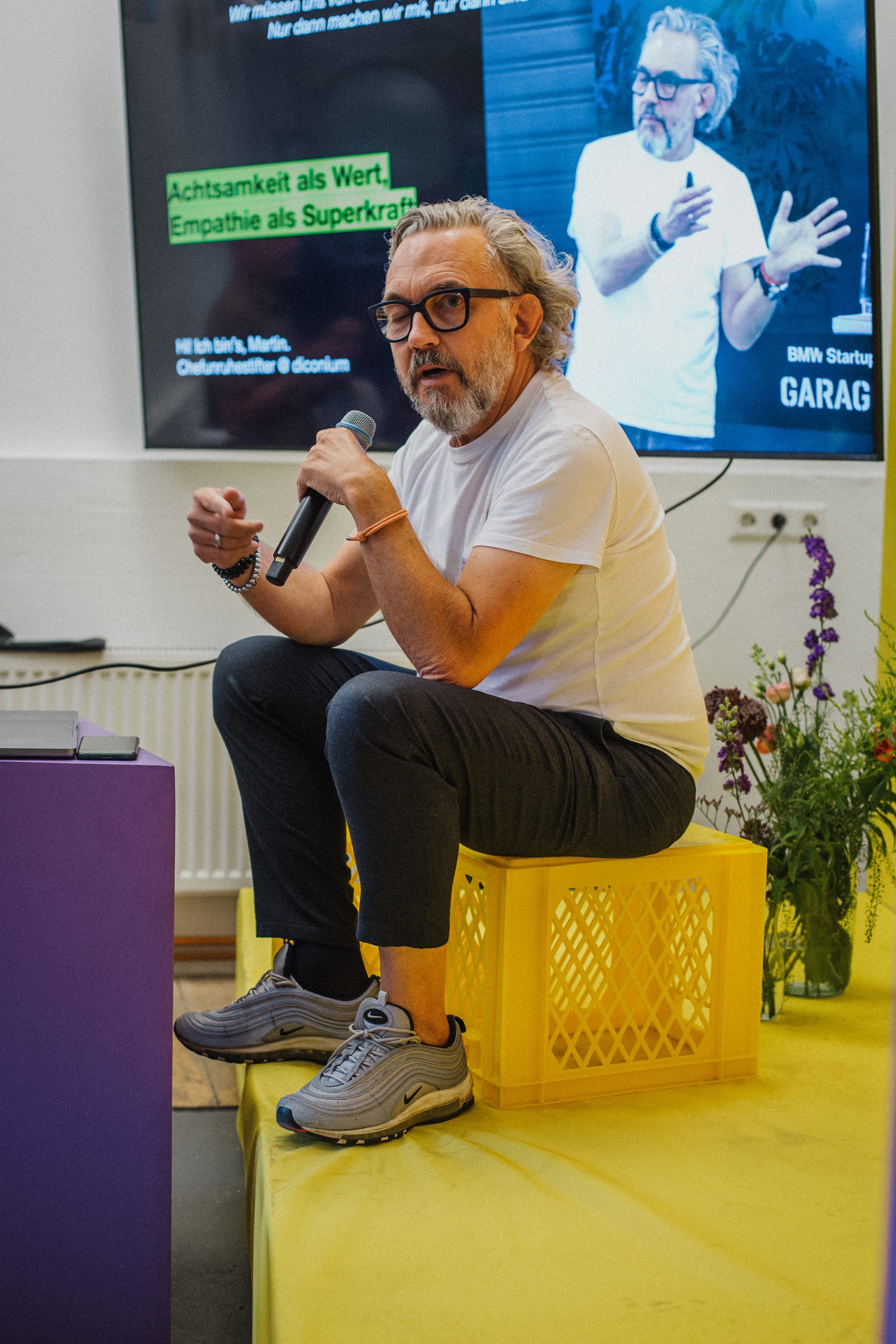 Martin Cserba (diconium) spricht mit Mikrofon auf gelber Kiste sitzend, Folie „Empathie als Superkraft“