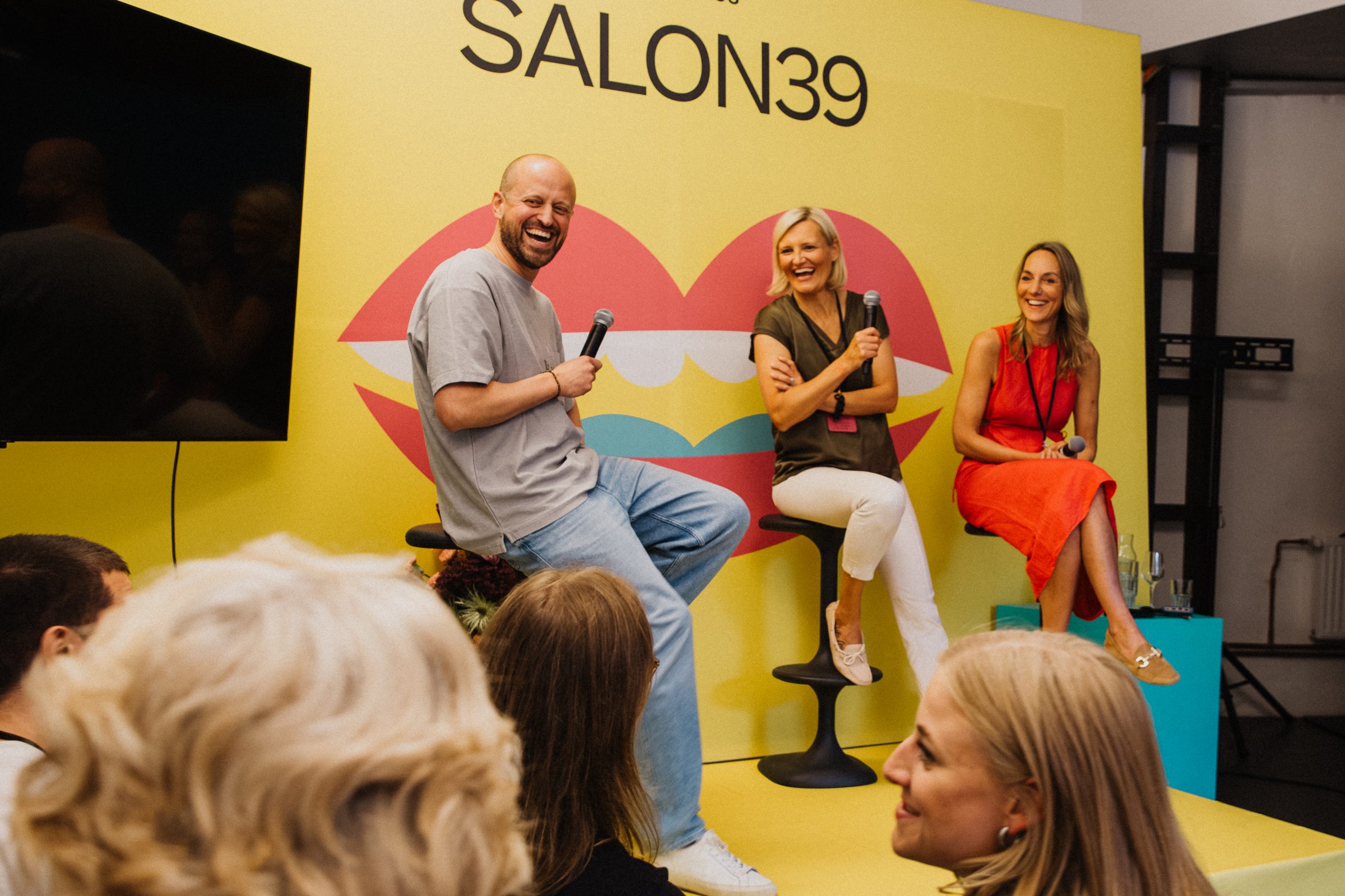 Three laughing panel guests seated on stools in front of the SALON39 stage backdrop.