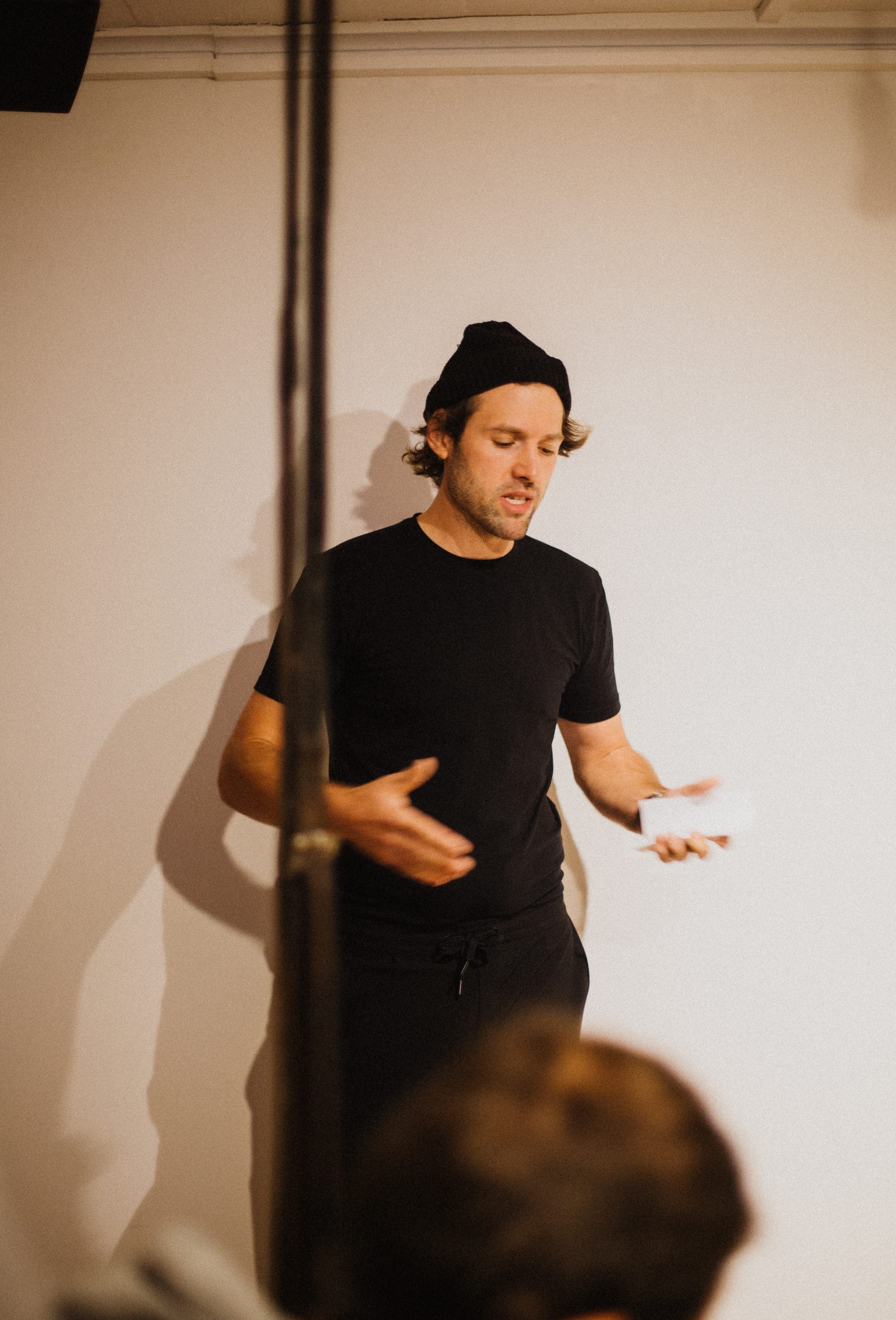 Speaker in a black beanie gives a talk, with the audience in the foreground