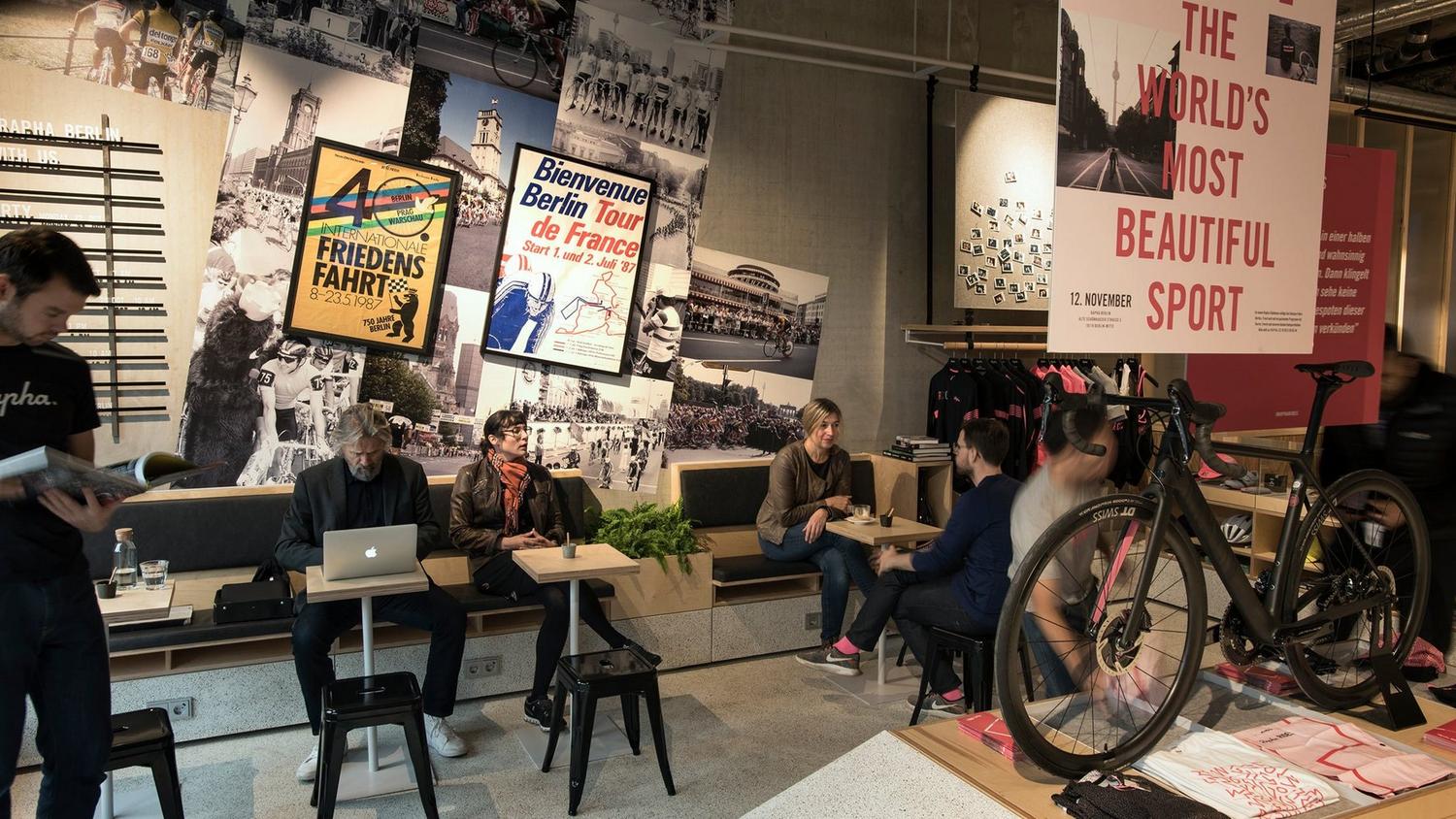 Lounge-Bereich mit Radsport-Postern, Sitzgruppen und ausgestelltem Rennrad in einem Rapha-Store