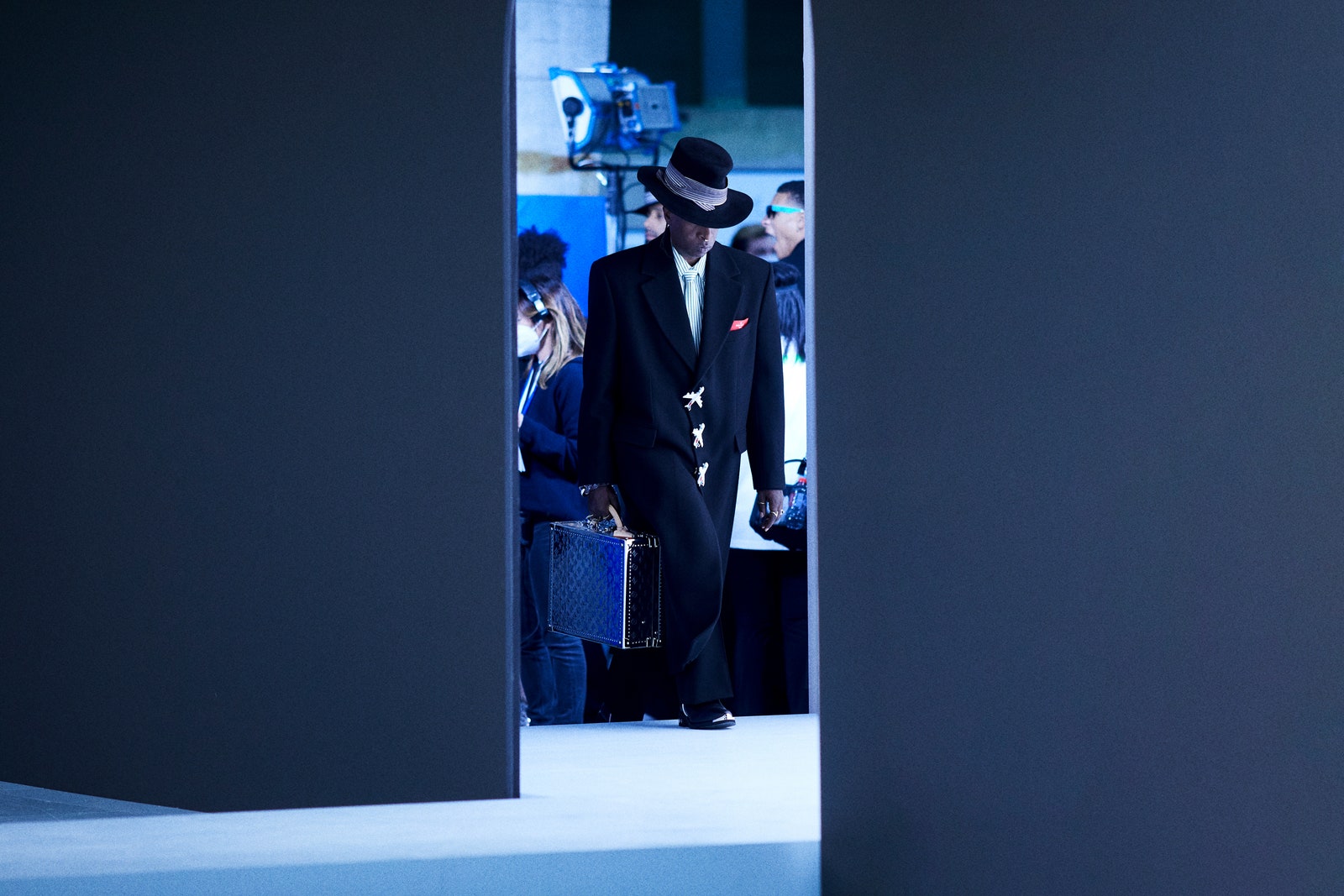 Model mit schwarzem Mantel, Hut und Louis-Vuitton-Koffer läuft über den Laufsteg der Fall-Winter-2021-Show.