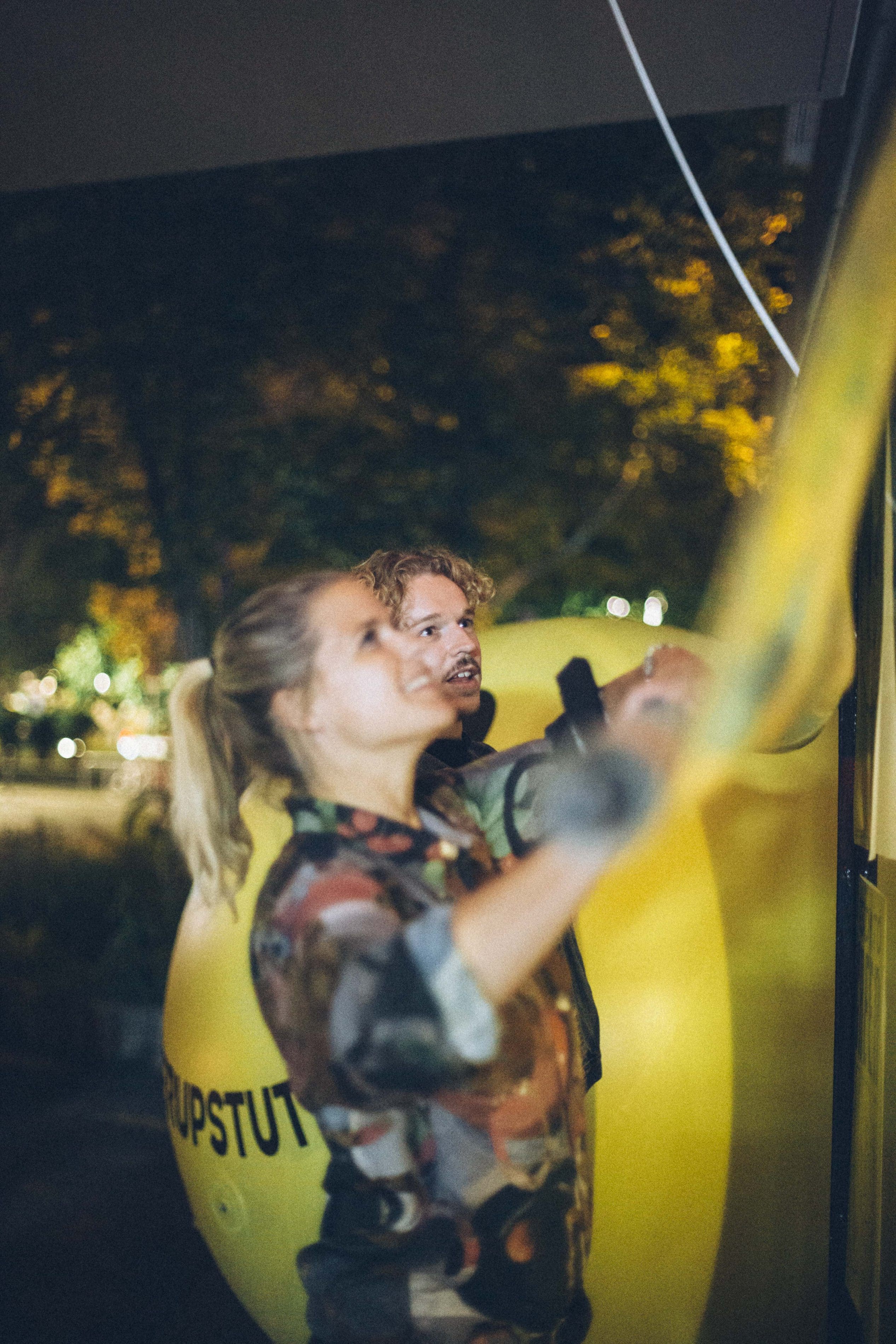 Two people fasten a rope to the giant yellow #CheerUpStuttgart balloon at night