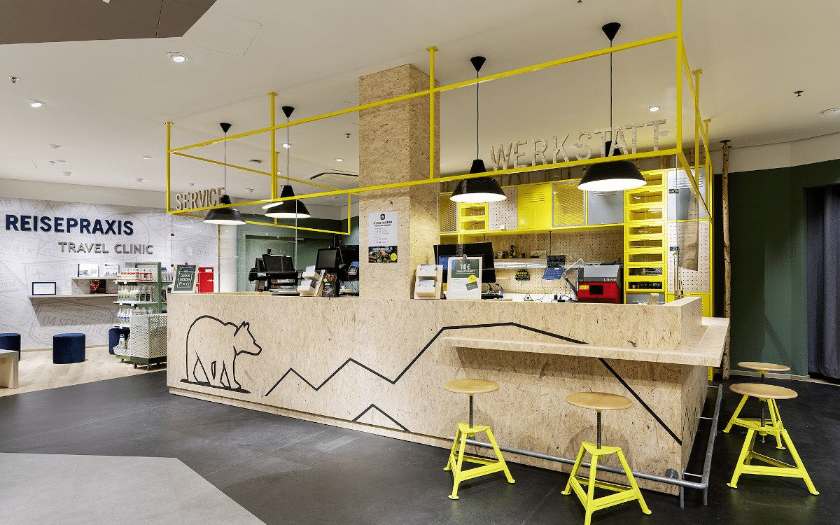 The “Reisepraxis Travel Clinic” service counter, built from OSB board with a bear illustration and a yellow tube frame.
