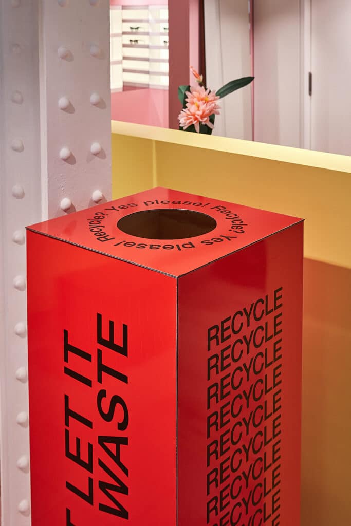 Roter Recycling-Behälter mit Aufschrift „Let it waste – Recycle“ im Ladeninterieur.