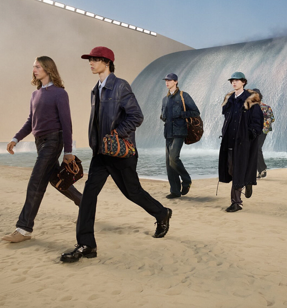 Models walking across a sand runway in front of a wave-shaped backdrop at the Louis Vuitton menswear show