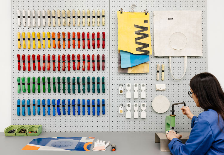 An employee works at a bench in front of a wall of colorful truck-tarp strips at FREITAG