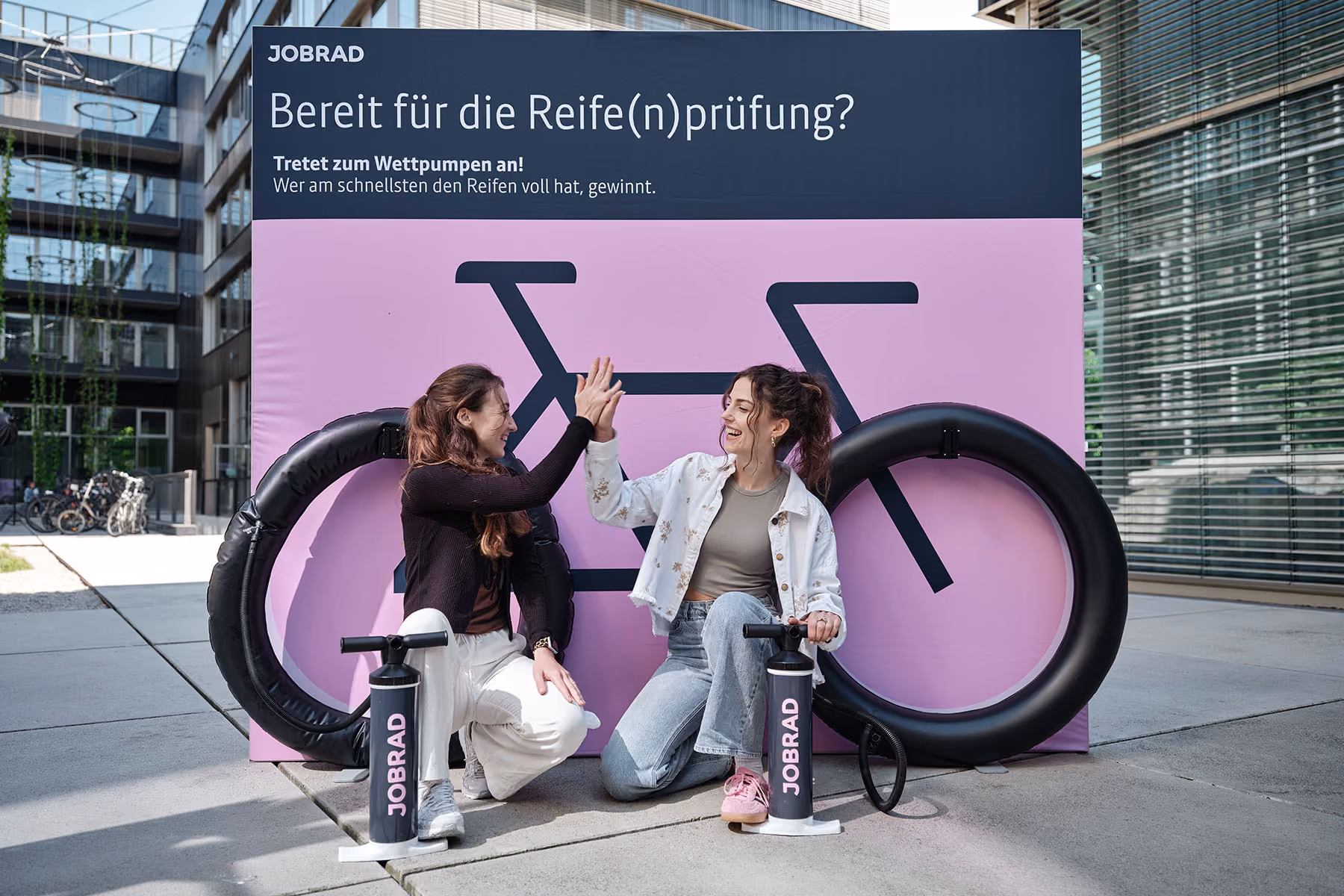 Zwei Frauen klatschen sich beim JobRad-Wettpumpen an übergroßen Reifen ab