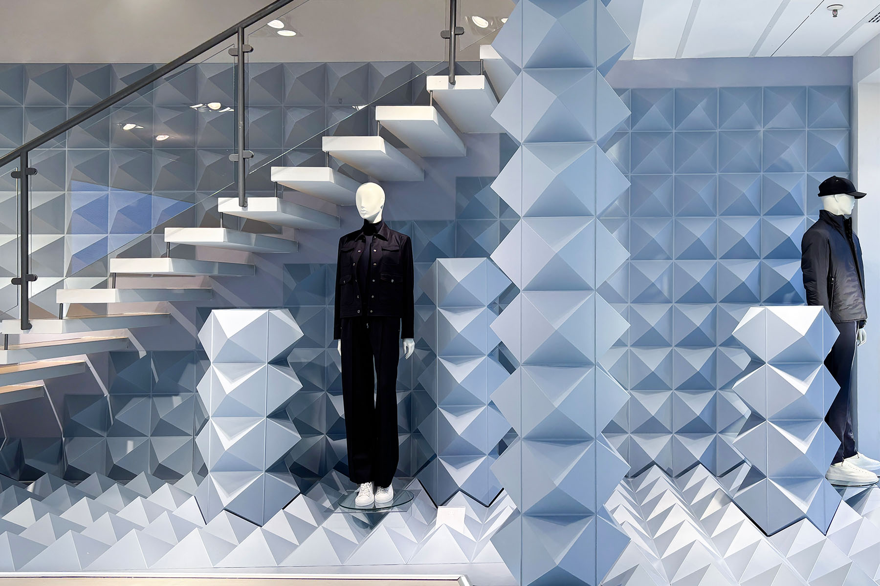 Zwei Mannequins vor der blauen Pyramidenwand unterhalb der Skulpturtreppe im BOGNER-Store