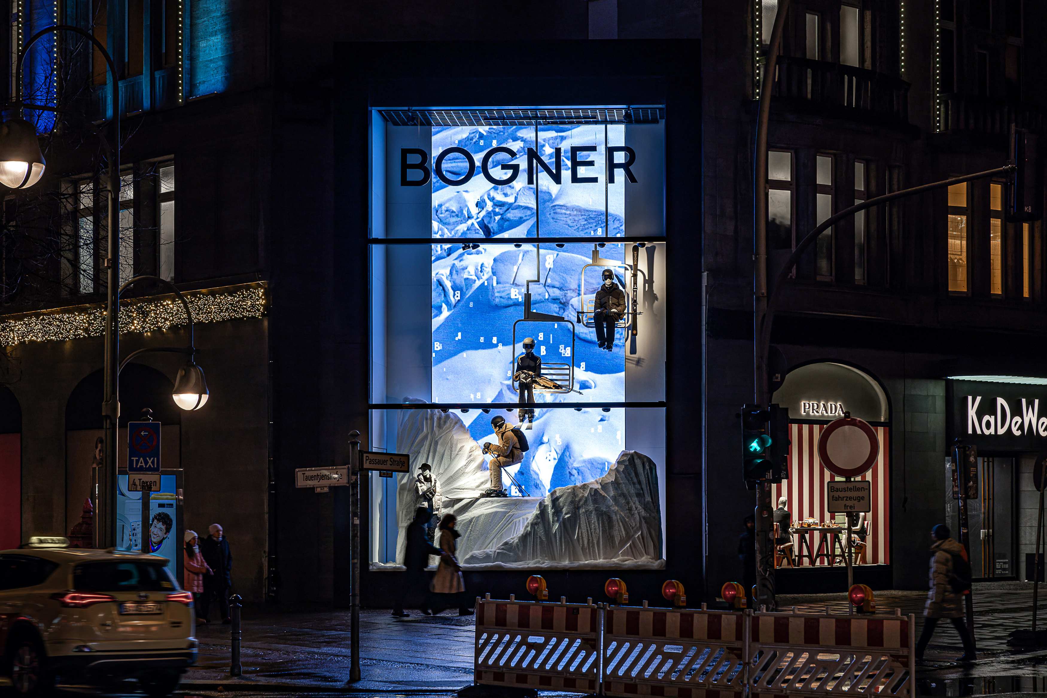 BOGNER-Schaufenster im KaDeWe: beleuchtete Berglandschaft mit Gondel, Passanten auf der Straße davor.