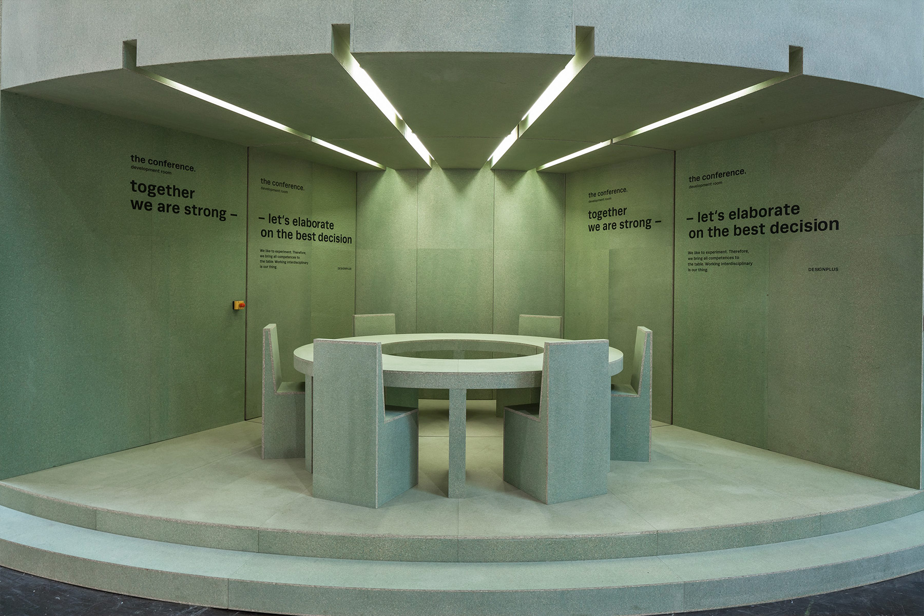 Rundes Bar-Element im Zentrum des Designplus-Messestands mit Slogans wie „together we are strong” an den mattgrünen Wänden.