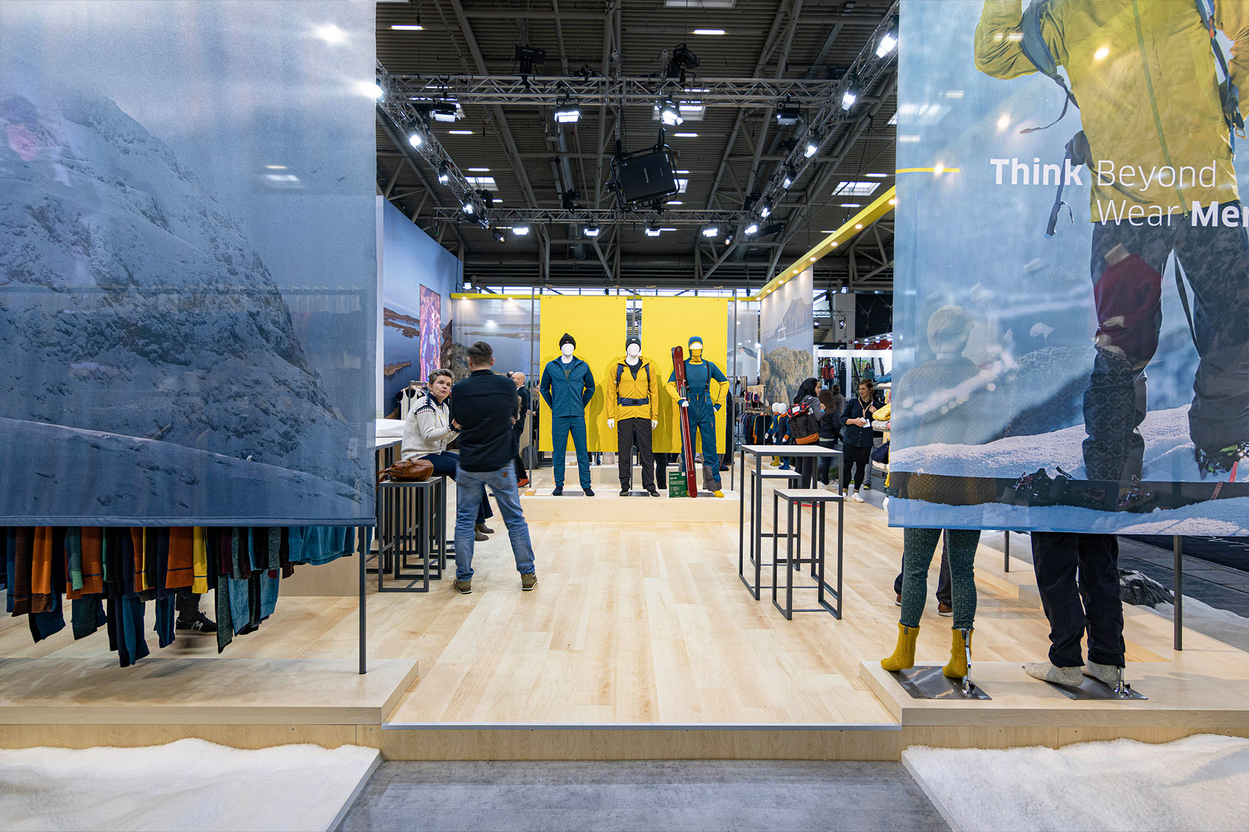 Devold-Messestand mit Mannequins in Wintersportbekleidung und Panoramafotos vor gelber Wand.