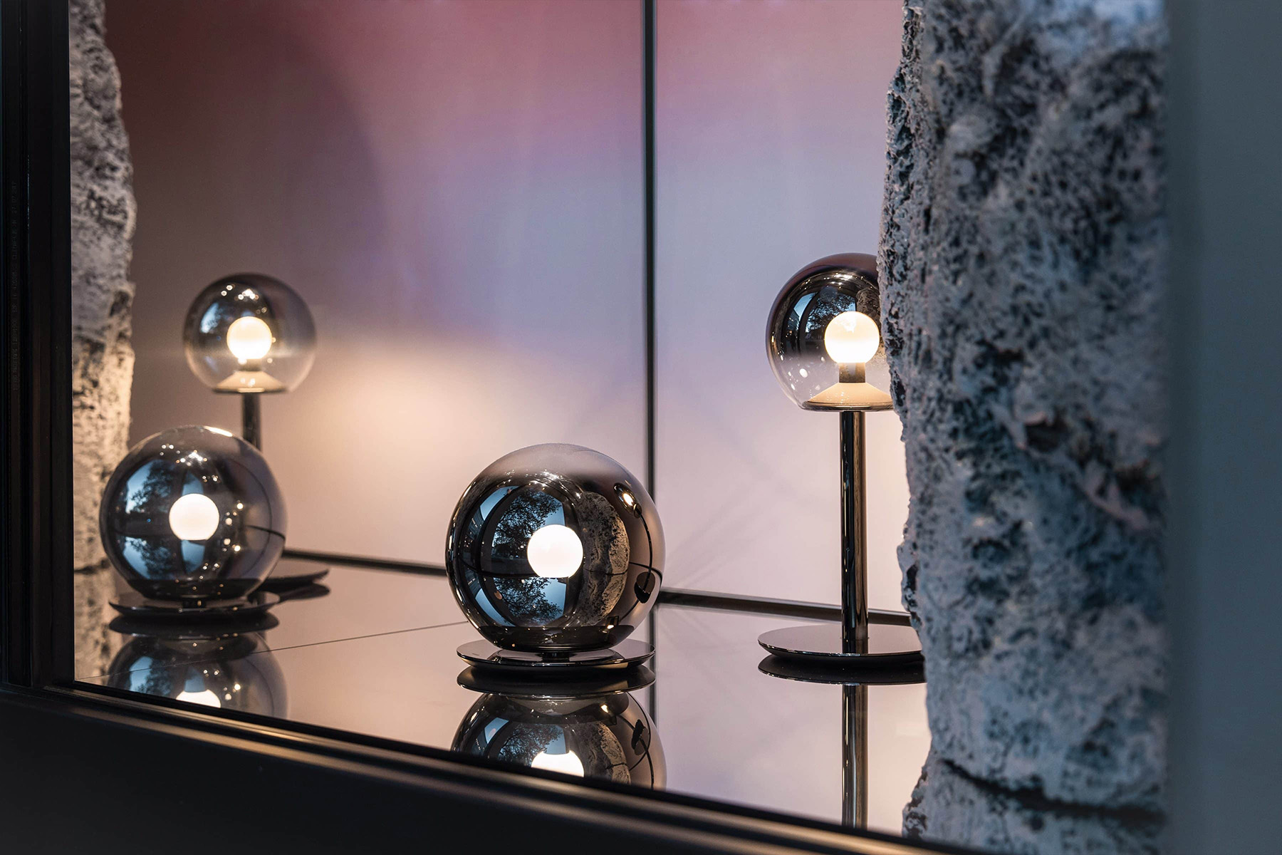 Three spherical Occhio lamps with reflections in front of a rock formation in the "Luna" window