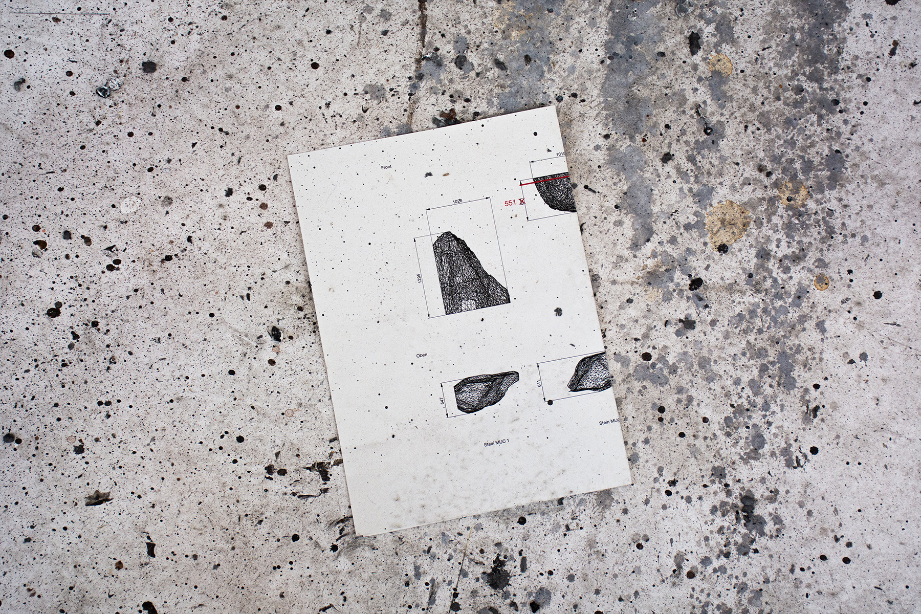Technical drawing with rock sketches lying on a speckled concrete floor, a planning detail for the Occhio installation