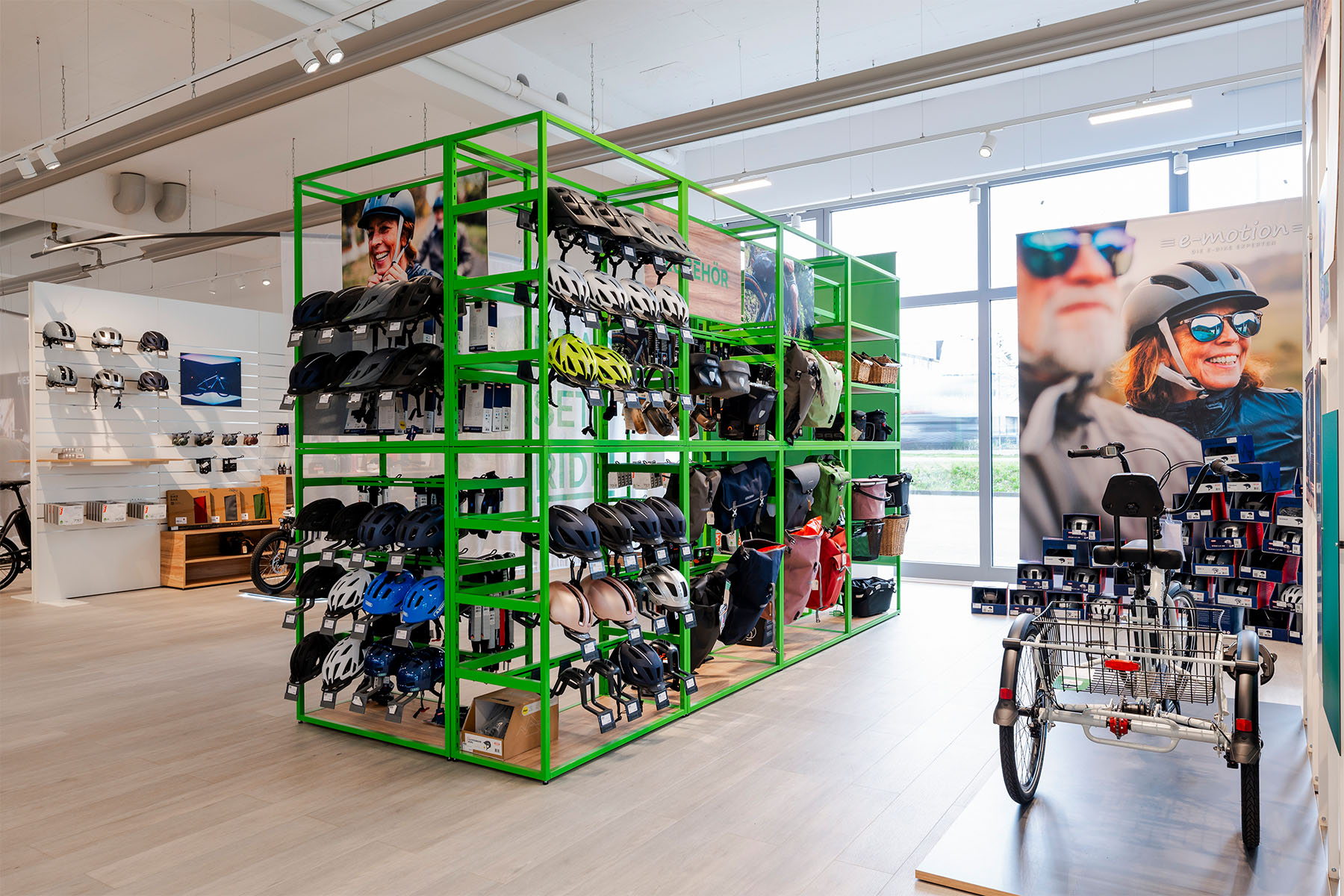 Green wire-frame shelving unit stocked with helmets and accessories in front of a large cyclist mural